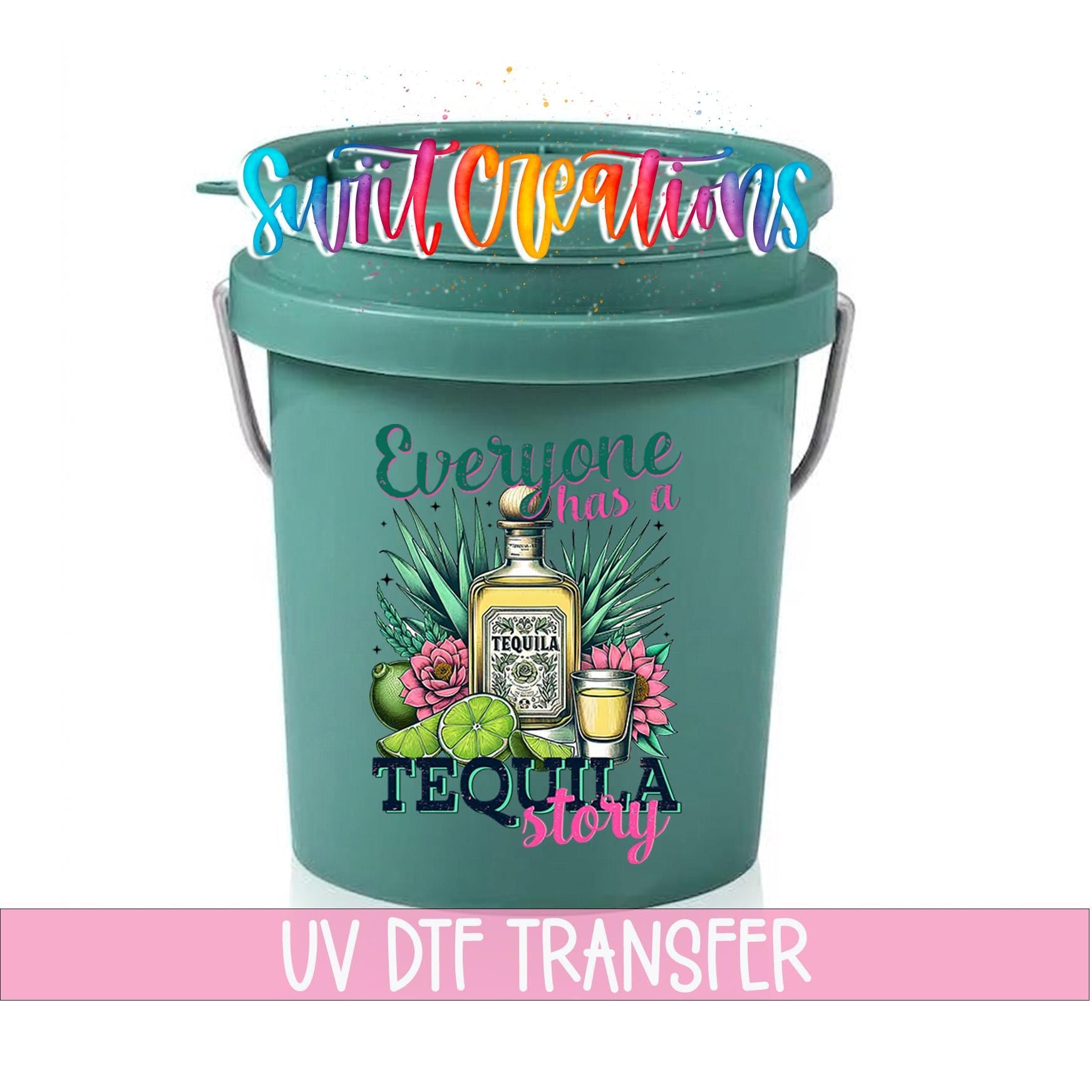 A green bucket with a printed design of a tequila bottle and various tequila-related items, along with the text "Everyone has a TEQUILA STORY" and "UV DFT TRANSFER".