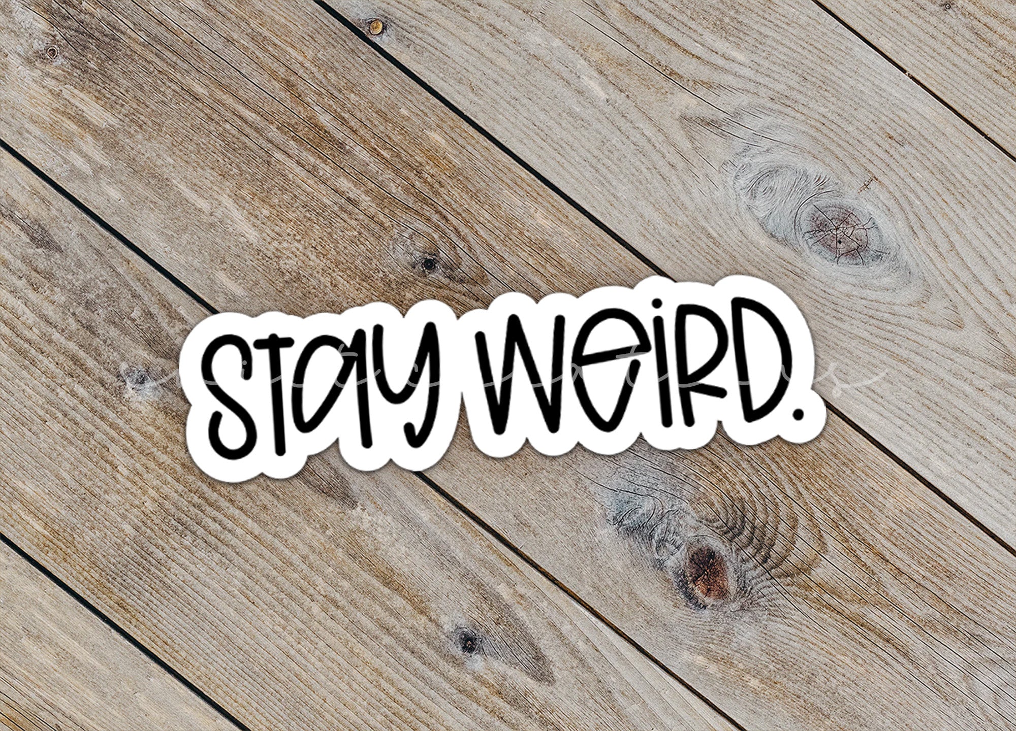 a sticker that says stay weird on a wooden surface