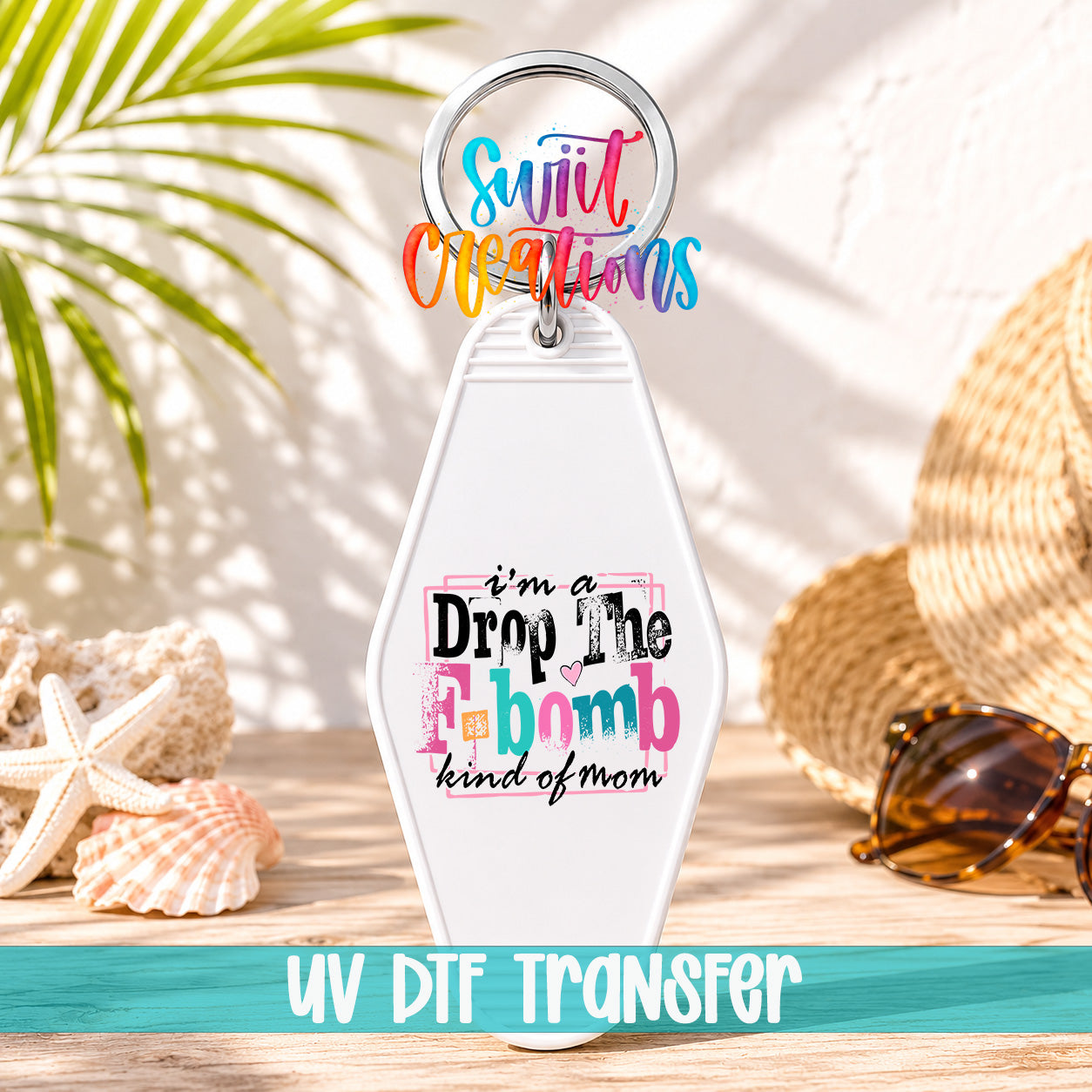 A keychain with a colorful design and text, placed on a wooden surface with sunglasses and a straw hat in the background.