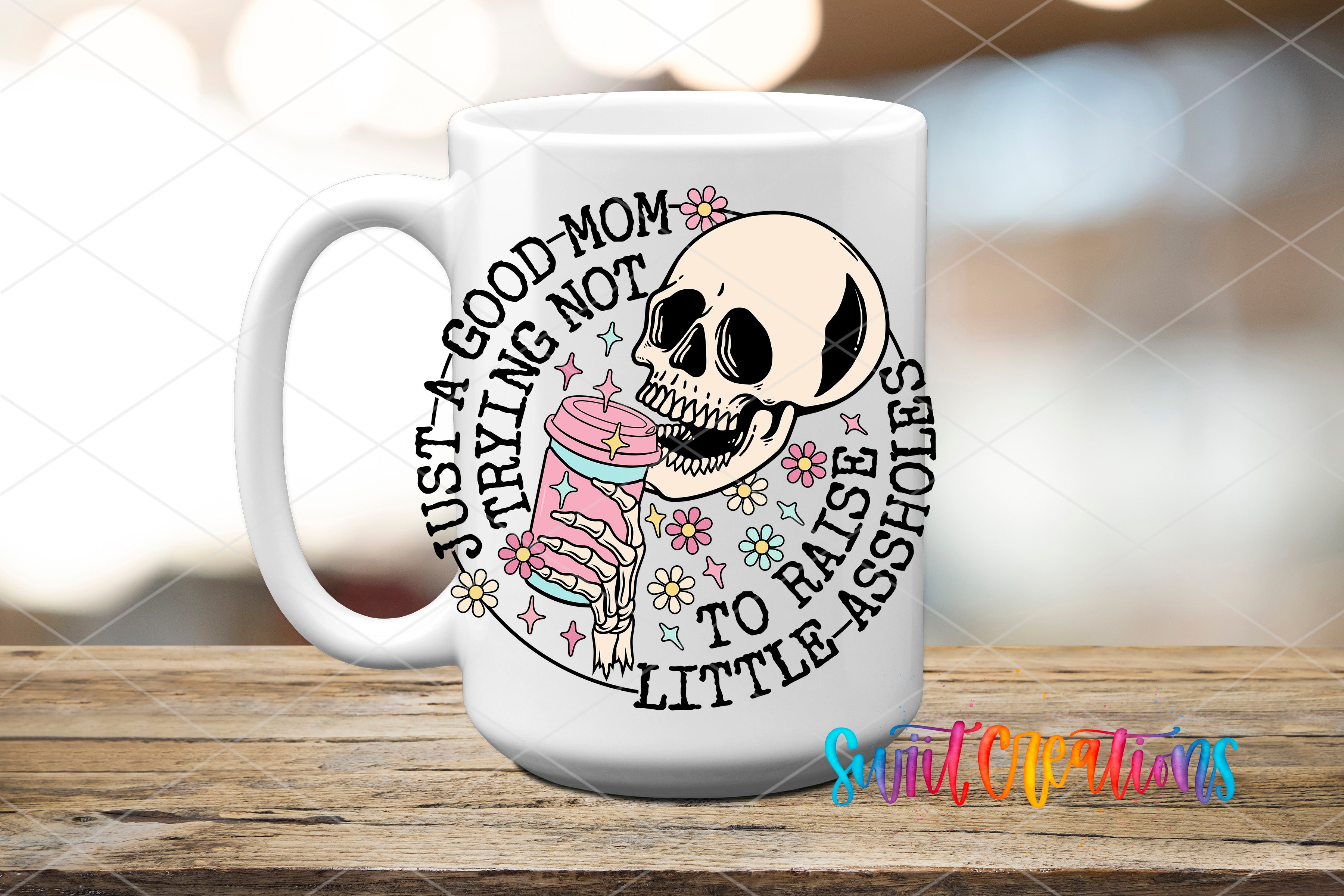 A white ceramic mug with a graphic design featuring a skull holding a cup with flowers, surrounded by text that reads "Just a good mom, not trying to raise a little assholes".