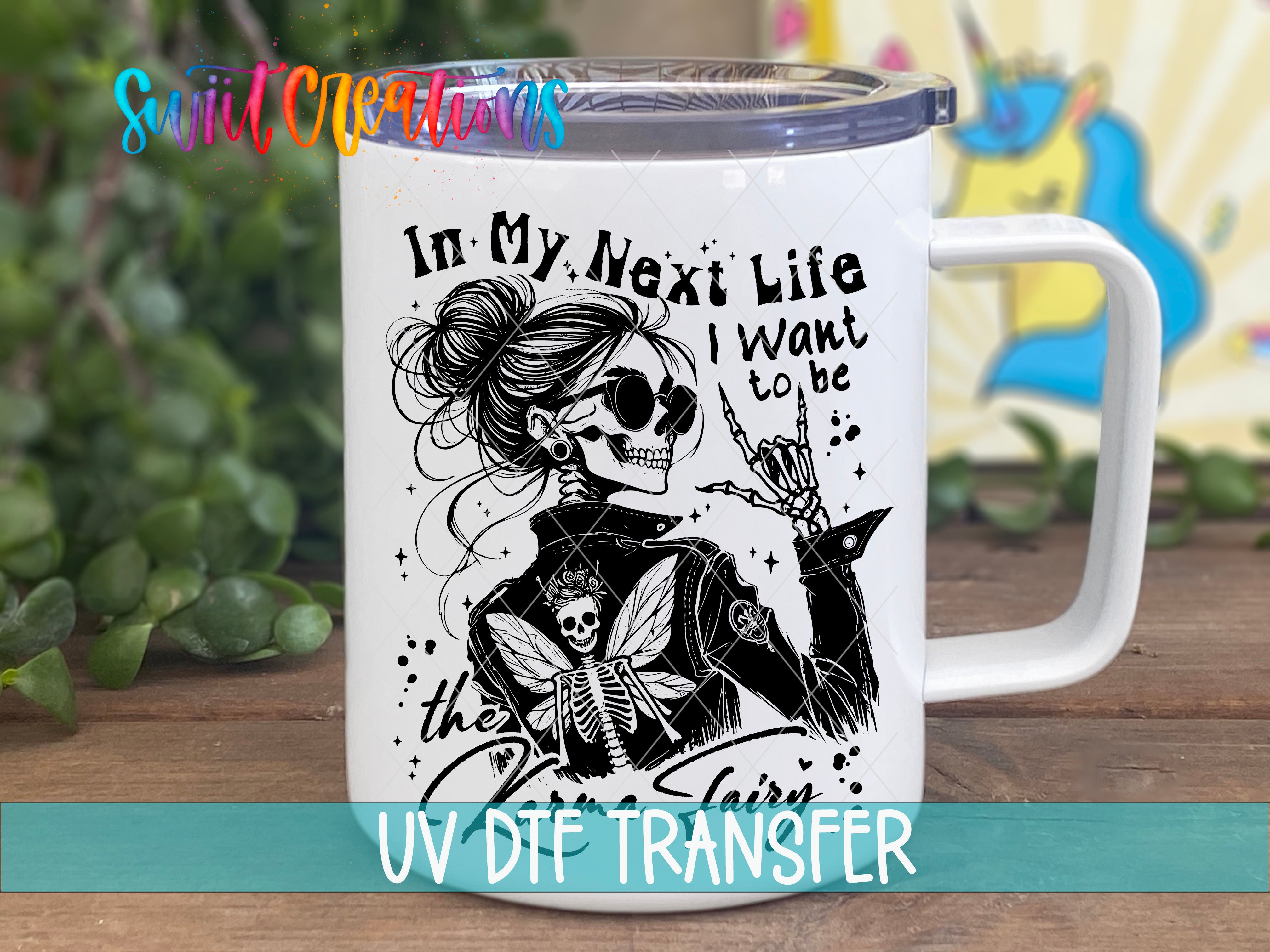 A white mug with a black and white illustration of a skeleton wearing sunglasses and holding a winged creature, accompanied by the text "In My Next Life I Want to be the fairy".