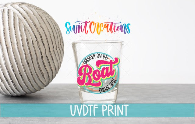 a shot glass with a colorful design and text, placed next to a white ball on a gray surface.