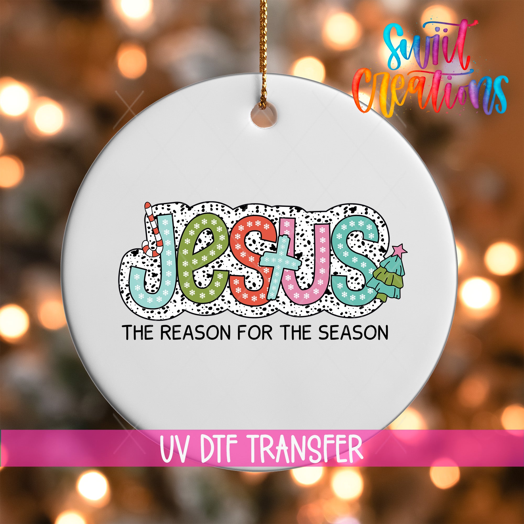 A white ornament with the word "JESUS" written in a colorful, playful font, along with the text "THE REASON FOR THE SEASON" below it. The ornament is hanging from a string, and there is a pink banner with the text "UV DDF TRANSFER" at the bottom.