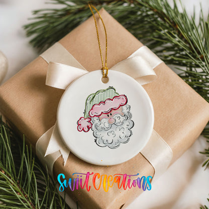 A ceramic ornament featuring a cartoon Santa Claus is displayed on a brown gift box, surrounded by pine branches.