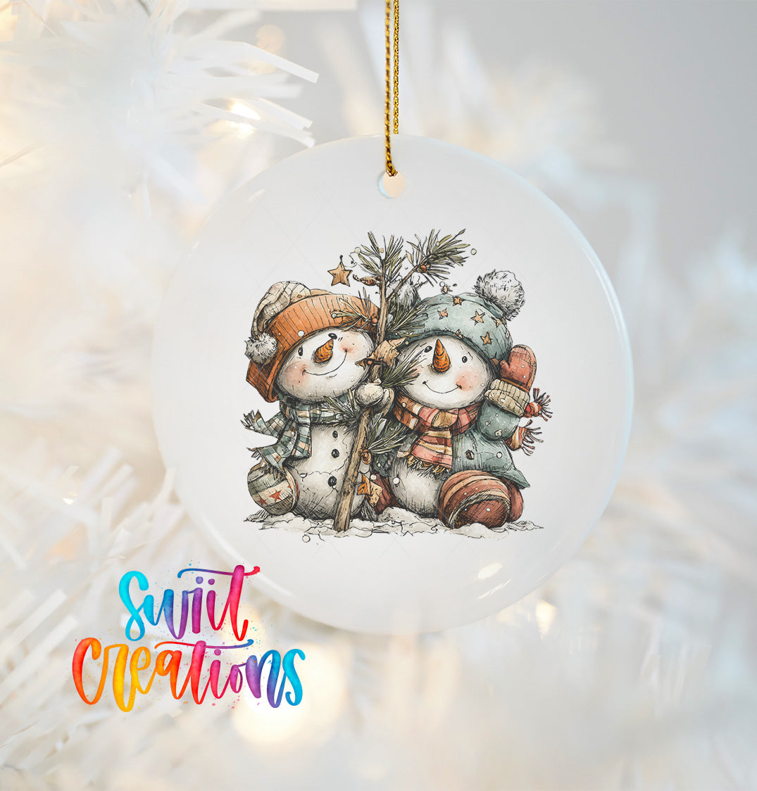 A white ornament featuring two snowmen, one wearing a green hat and the other a red hat, sitting together and smiling.