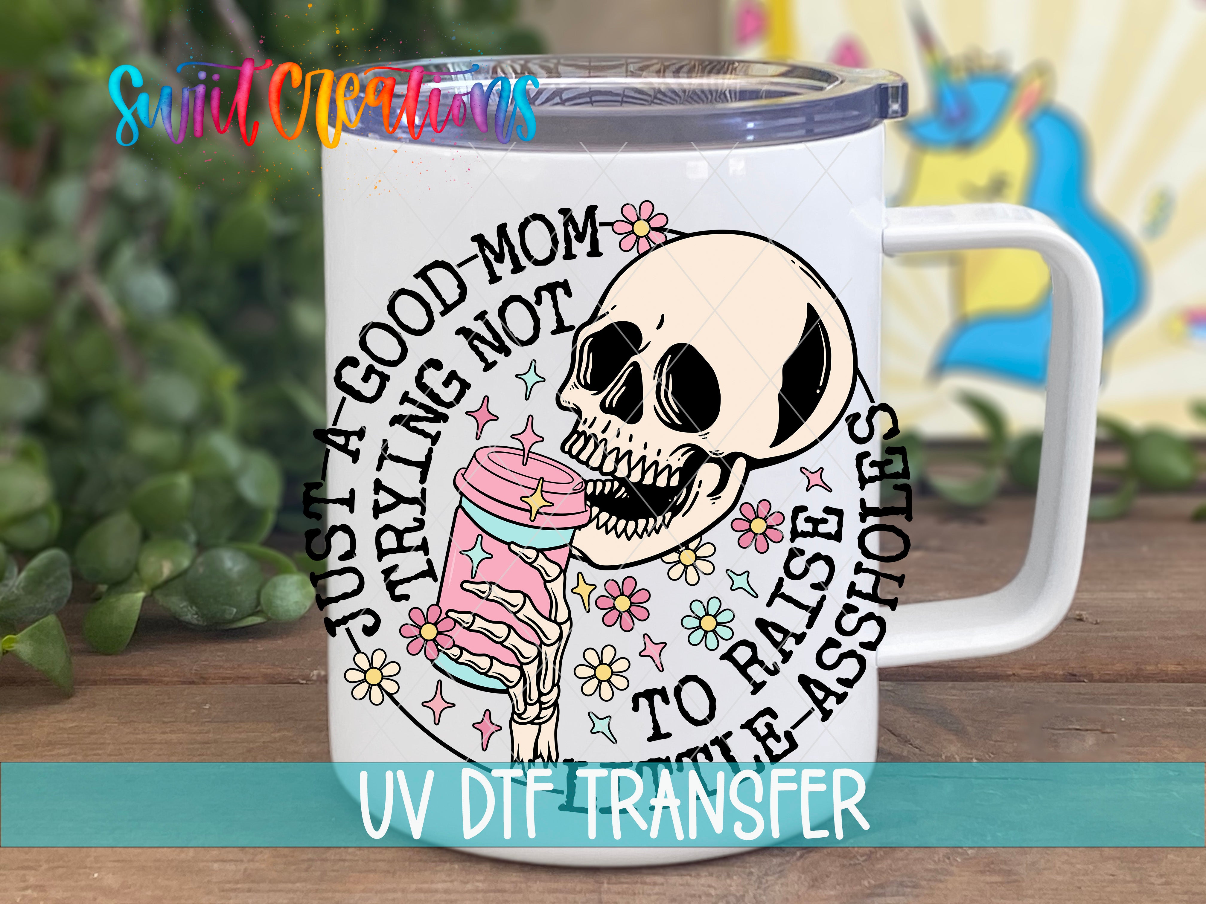 A white mug with a skull and floral design, along with text that says "Just a good mom to raise the assholes".