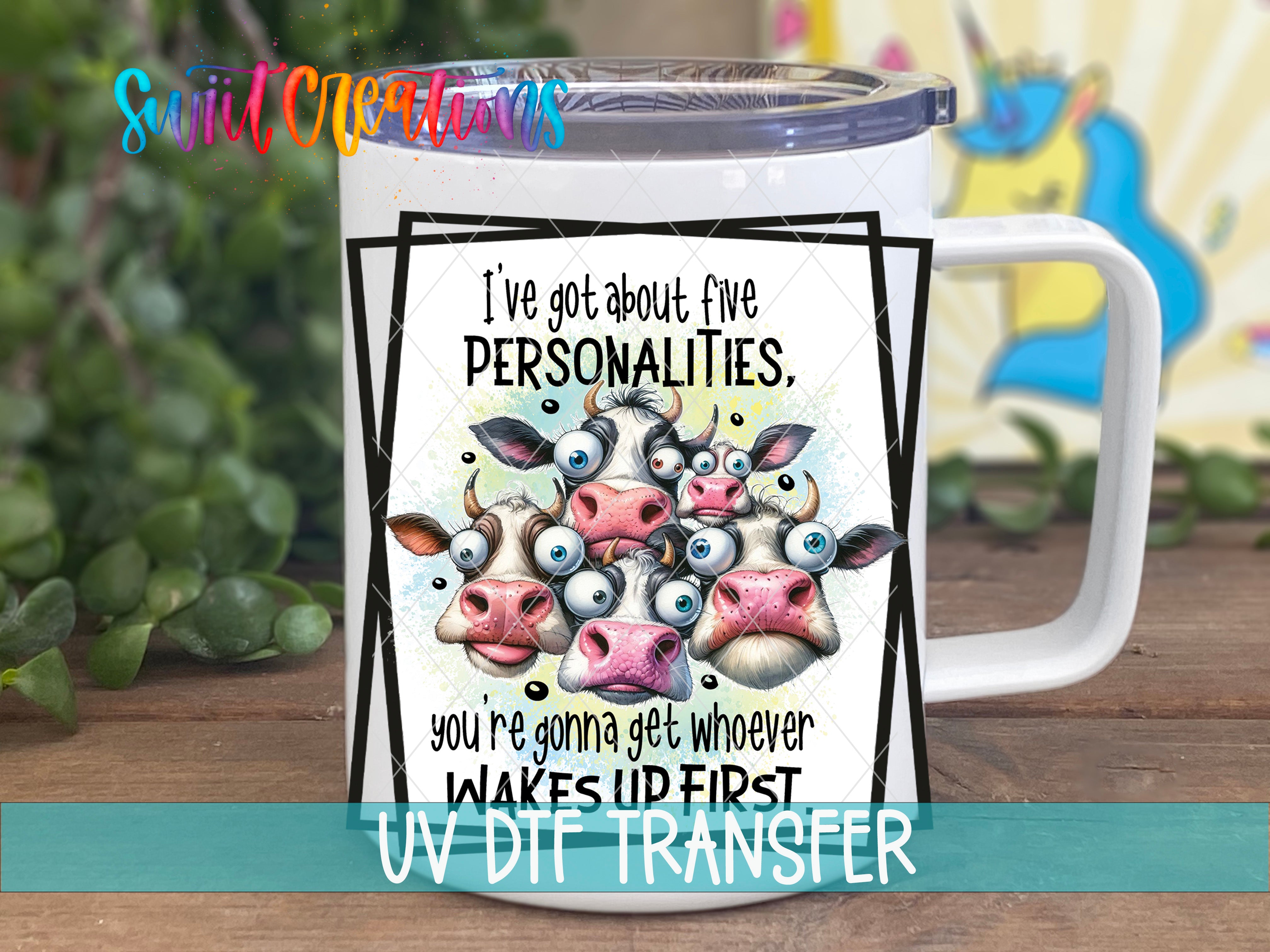 A white mug with a printed design featuring a group of cows with exaggerated features, including large eyes and horns. The text on the mug reads "I've got about five personalities. You're gonna get whoever WAKES UP FIRST".