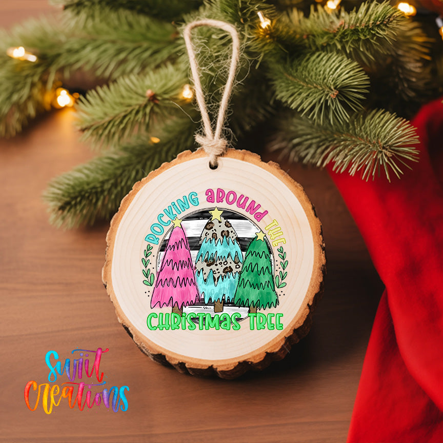 A wooden ornament with a colorful illustration of three Christmas trees hanging on a tree branch, surrounded by twinkling lights.