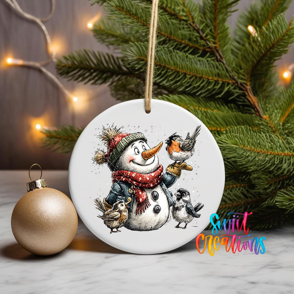 A white ornament featuring a snowman holding a bird and a small bird, surrounded by pine branches and twinkling lights.