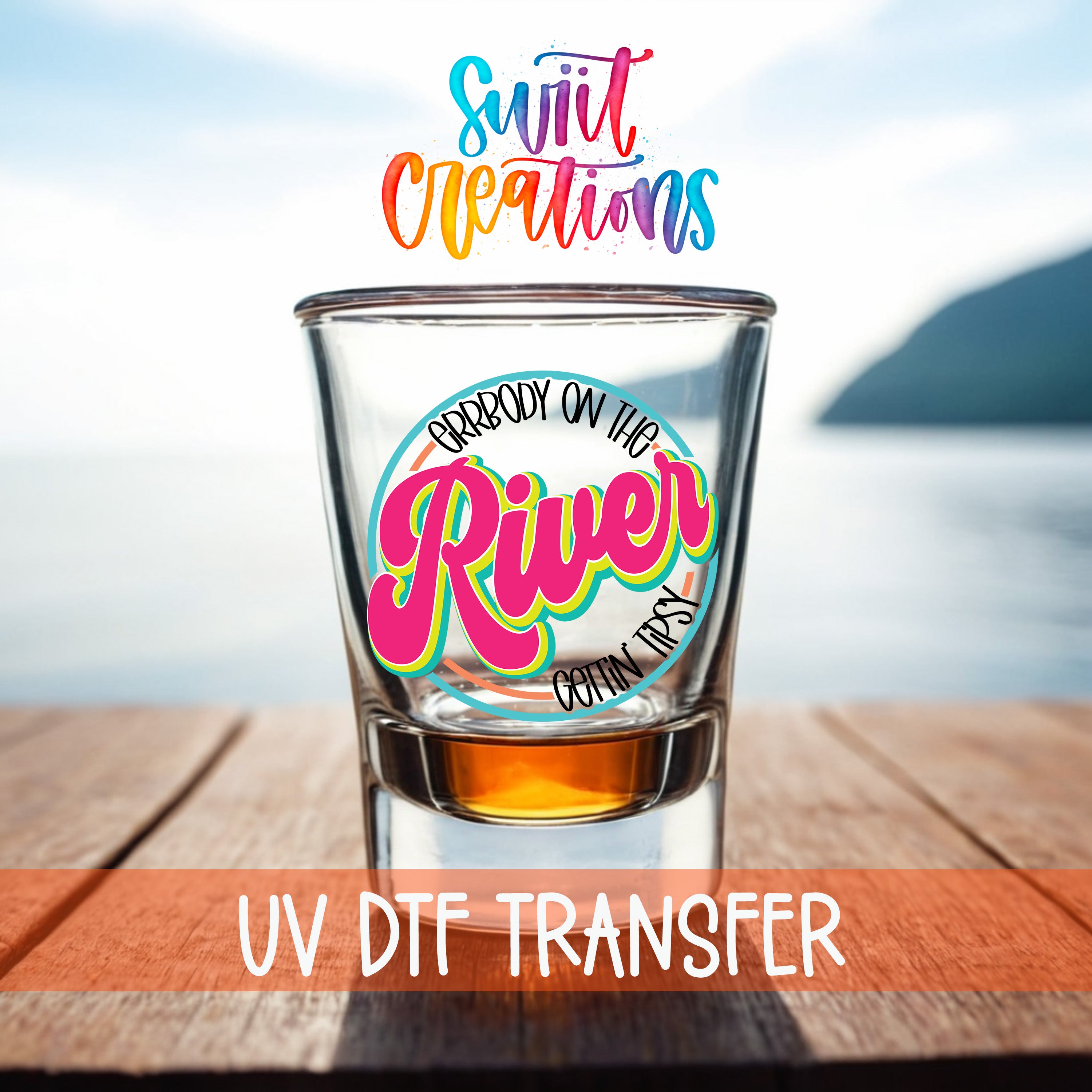 a shot glass with a colorful design on it, placed on a wooden surface with a body of water in the background.