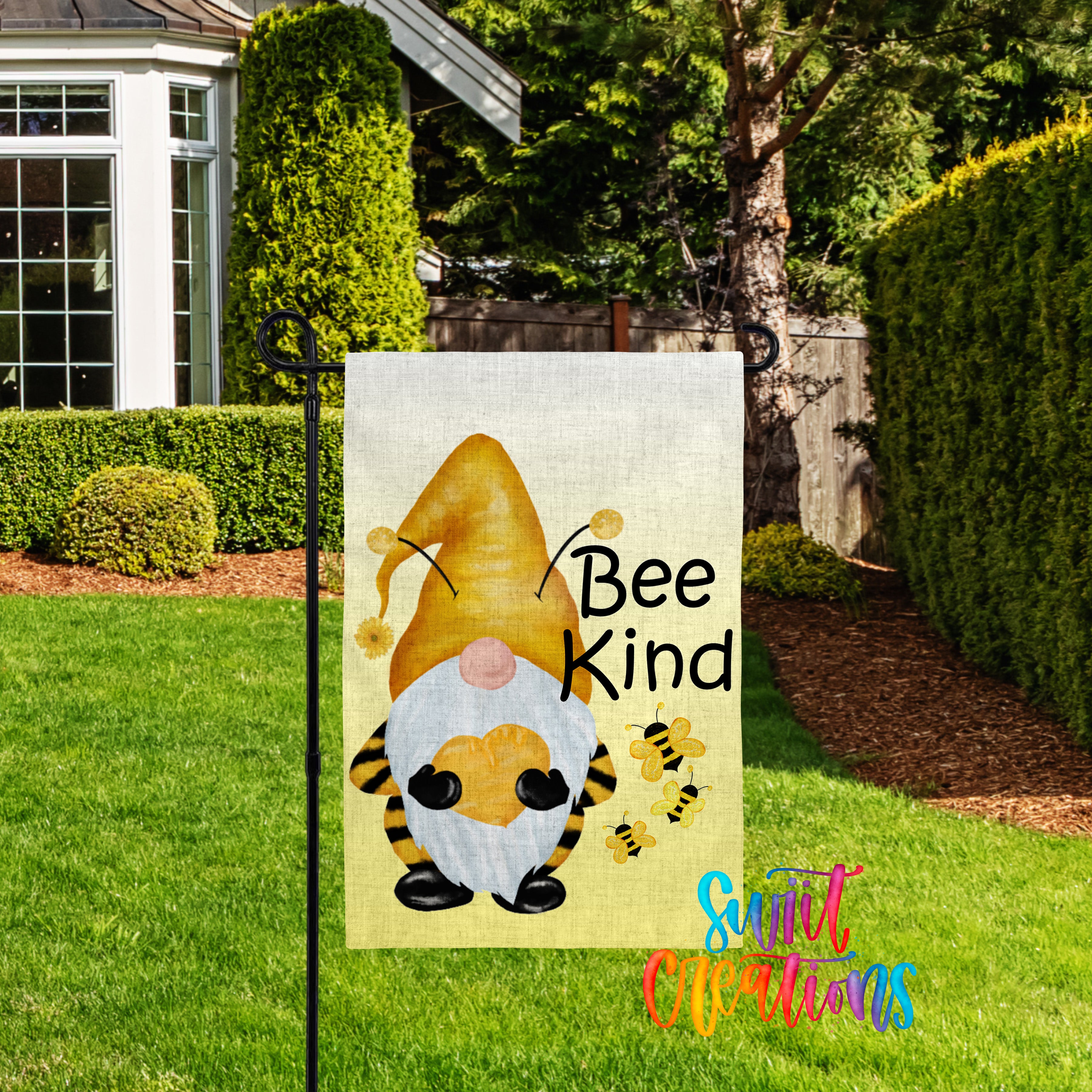 A garden gnome sign with the text "Bee Kind" and illustrations of bees, placed in a grassy yard with a house and trees in the background.