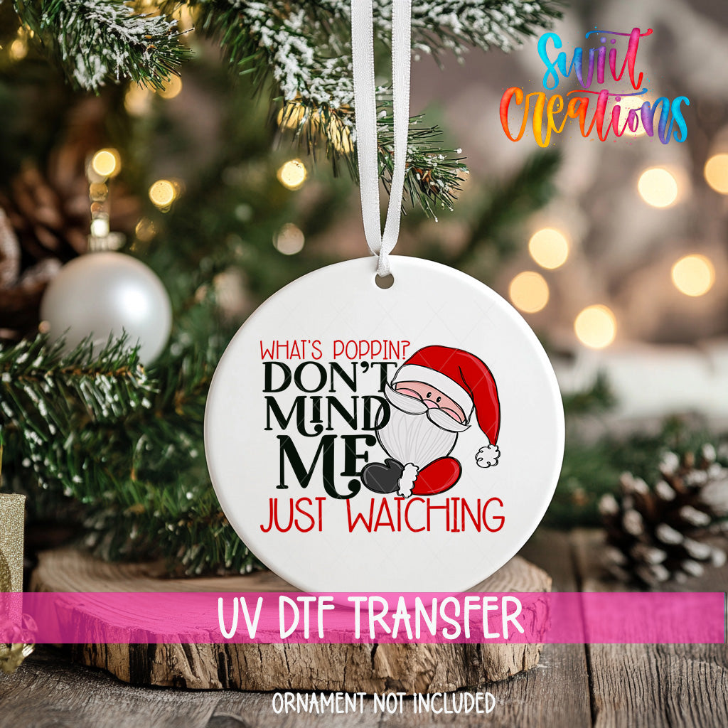 A white ornament with a Santa Claus design and text hanging on a Christmas tree.