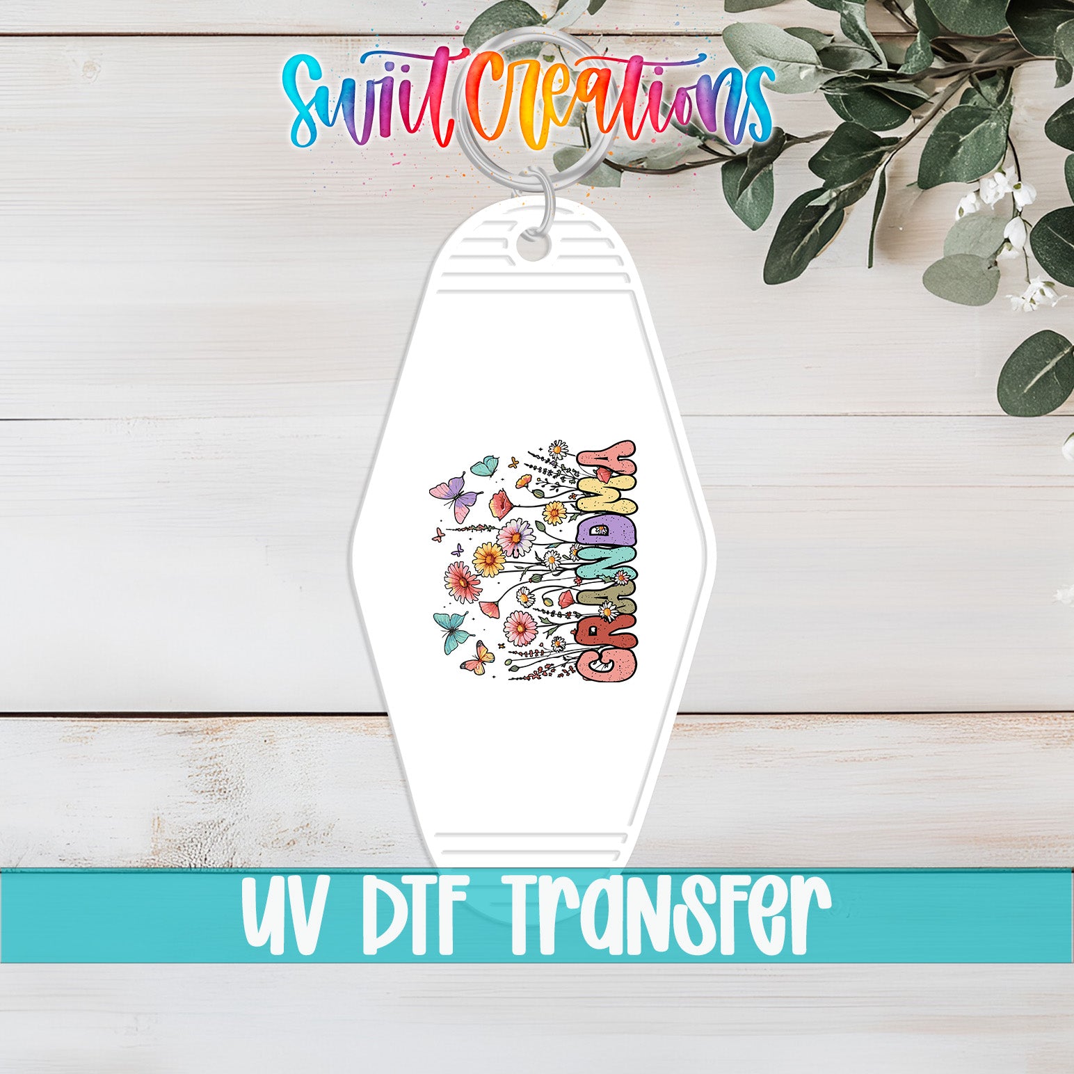 A keychain with a colorful floral design and the word "GRANDMA" printed on it, placed on a wooden surface with some greenery in the background.