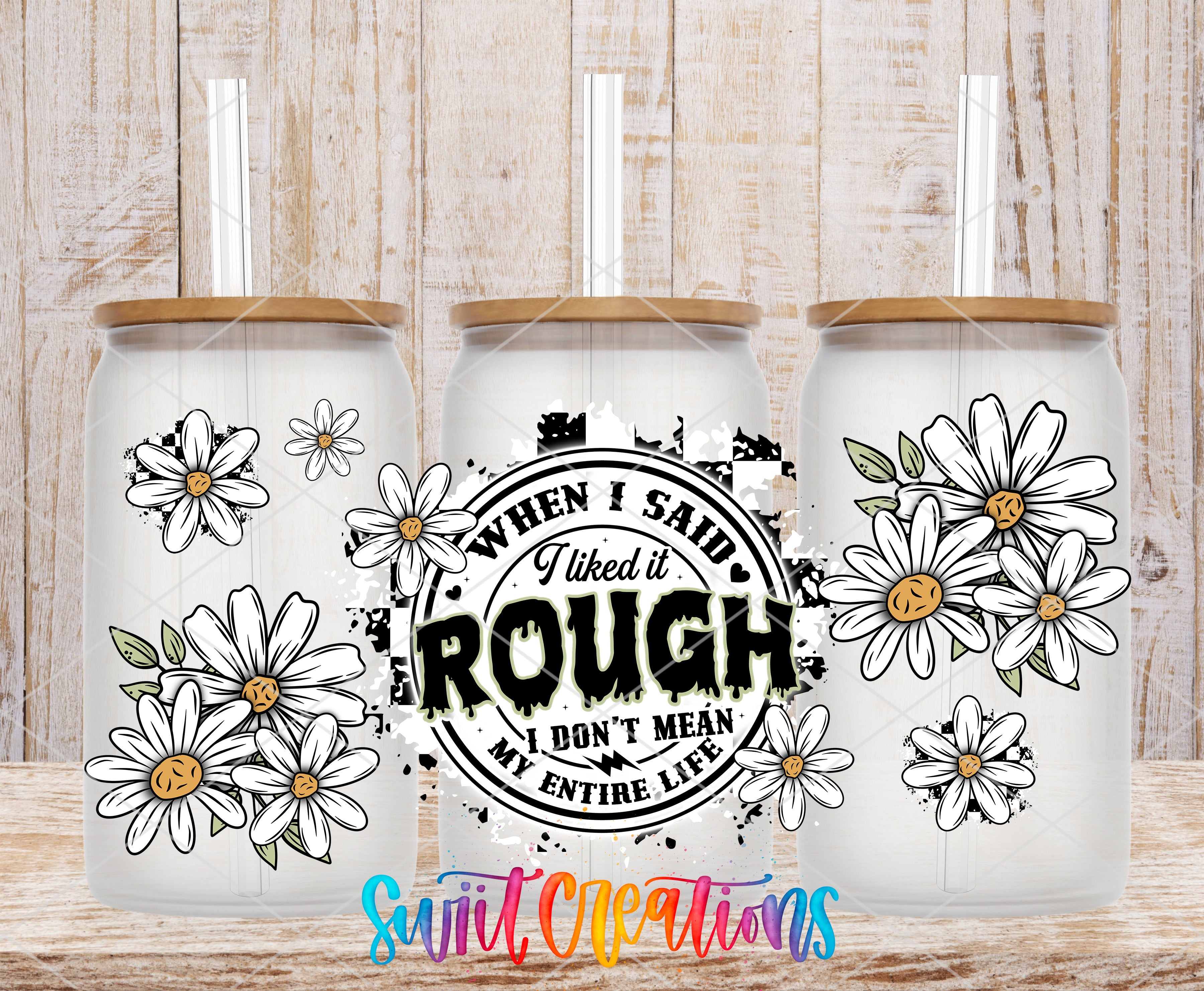 three glass tumblers with white daisy designs on them, placed on a wooden surface.
