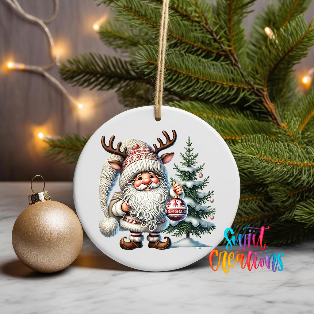 A white ceramic ornament featuring a Santa Claus figure holding a Christmas ornament and a Christmas tree, with a gold ornament and a string of lights in the background.