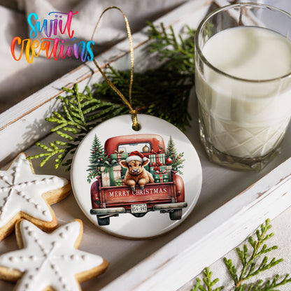 a Christmas ornament with a dog in a Santa hat, riding in a red truck carrying presents, and the text "Merry Christmas" on the back of the truck. The ornament is hanging from a gold string, and there is a glass of milk and two star-shaped cookies on a white tray in the background.