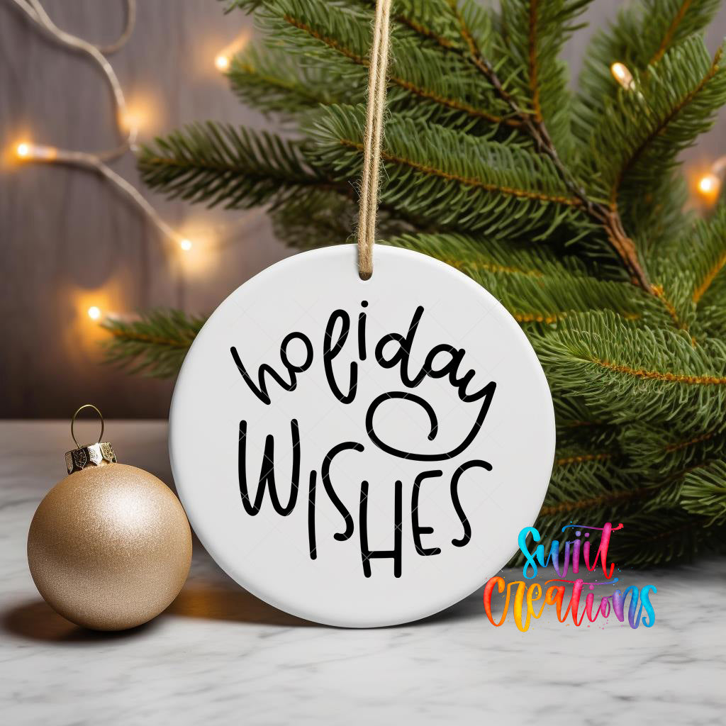 A white ornament with the text "Holiday Wishes" written on it, hanging from a string, is placed next to a gold ornament and a pine tree with twinkling lights in the background.