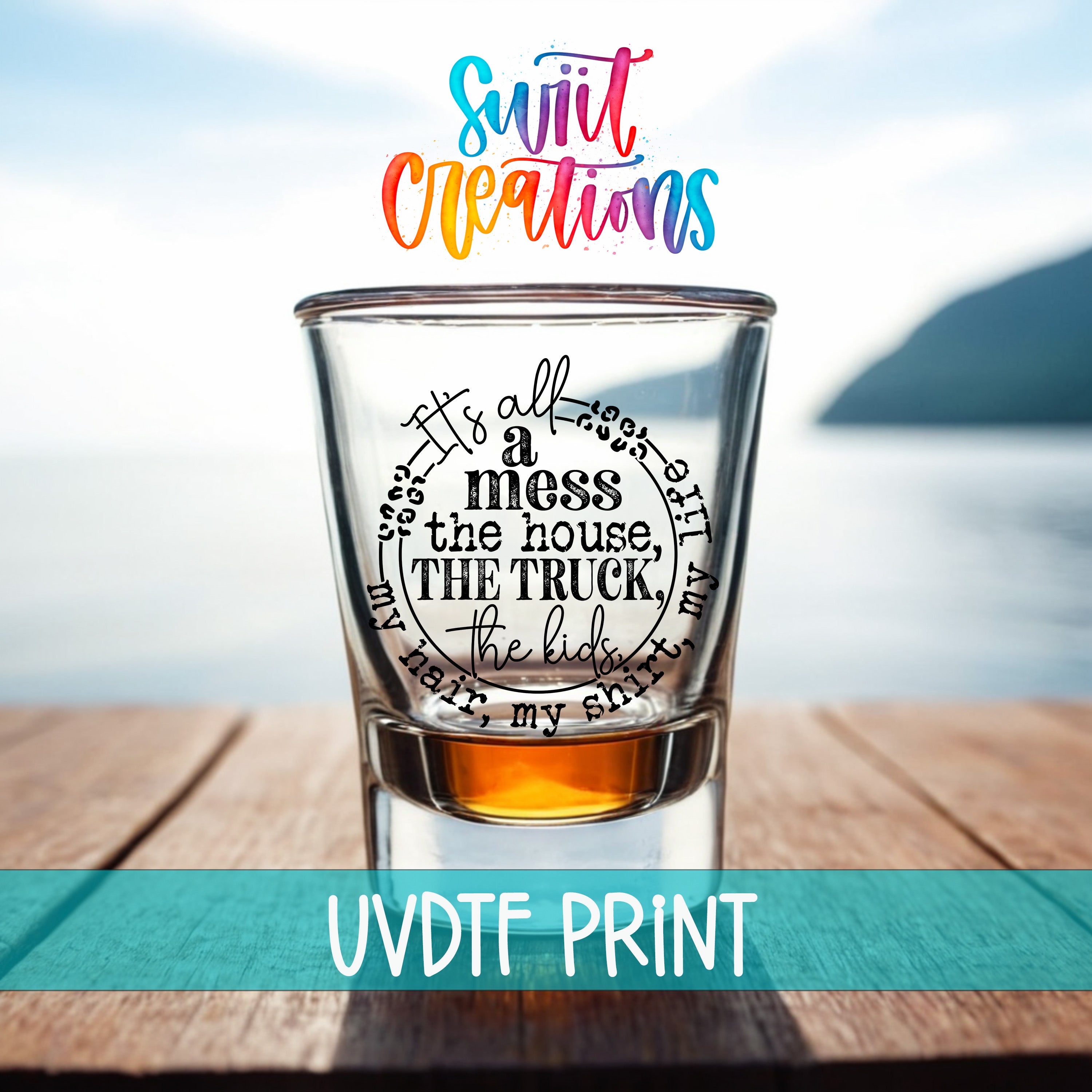 a shot glass with a humorous text printed on it, placed on a wooden surface with a body of water in the background.