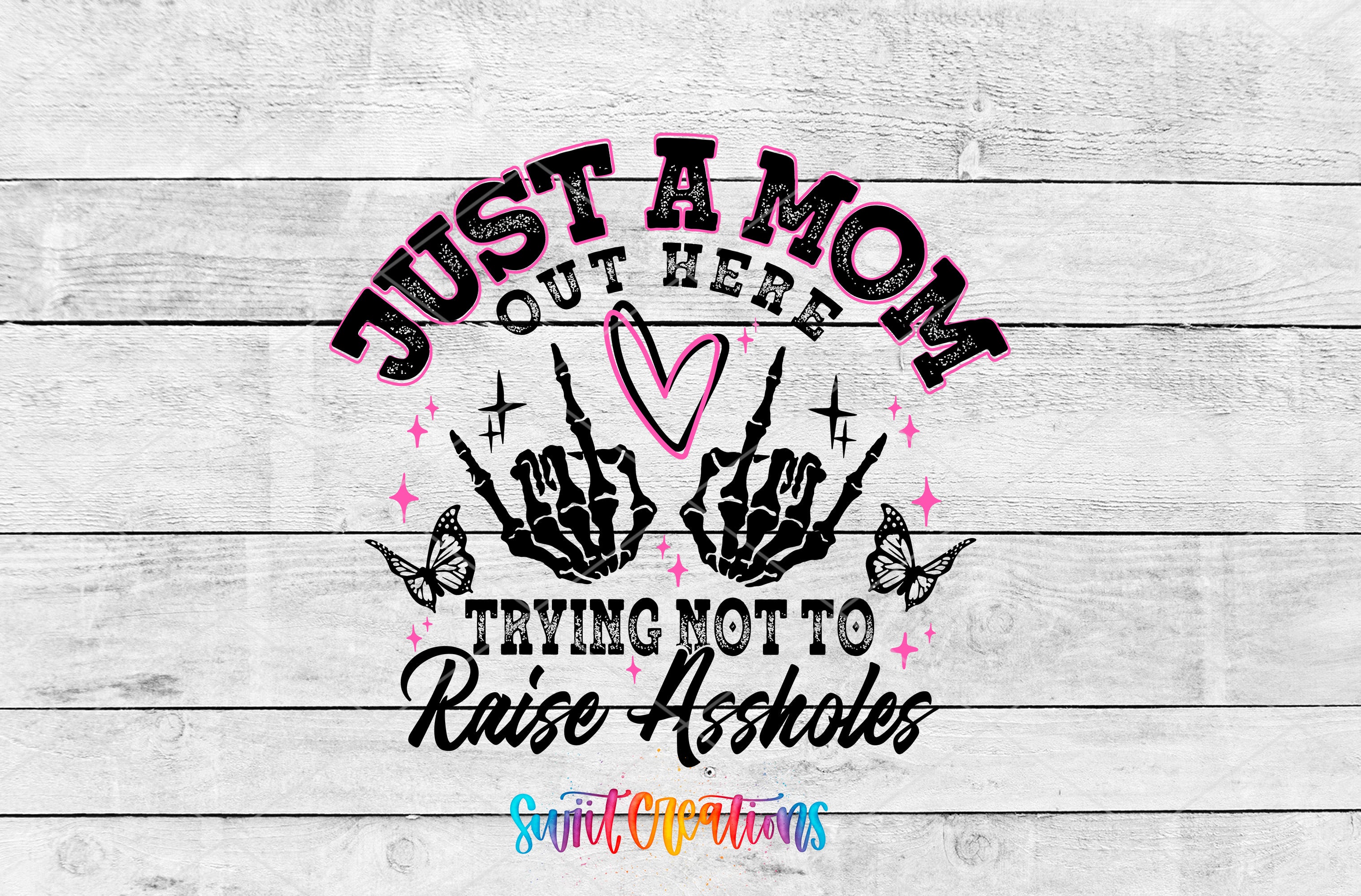 a graphic design with a text and skeleton hand graphic. The text reads "Just a mom out here trying not to raise assholes" and is surrounded by a skeleton hand and butterflies. The design is set against a white wooden background.