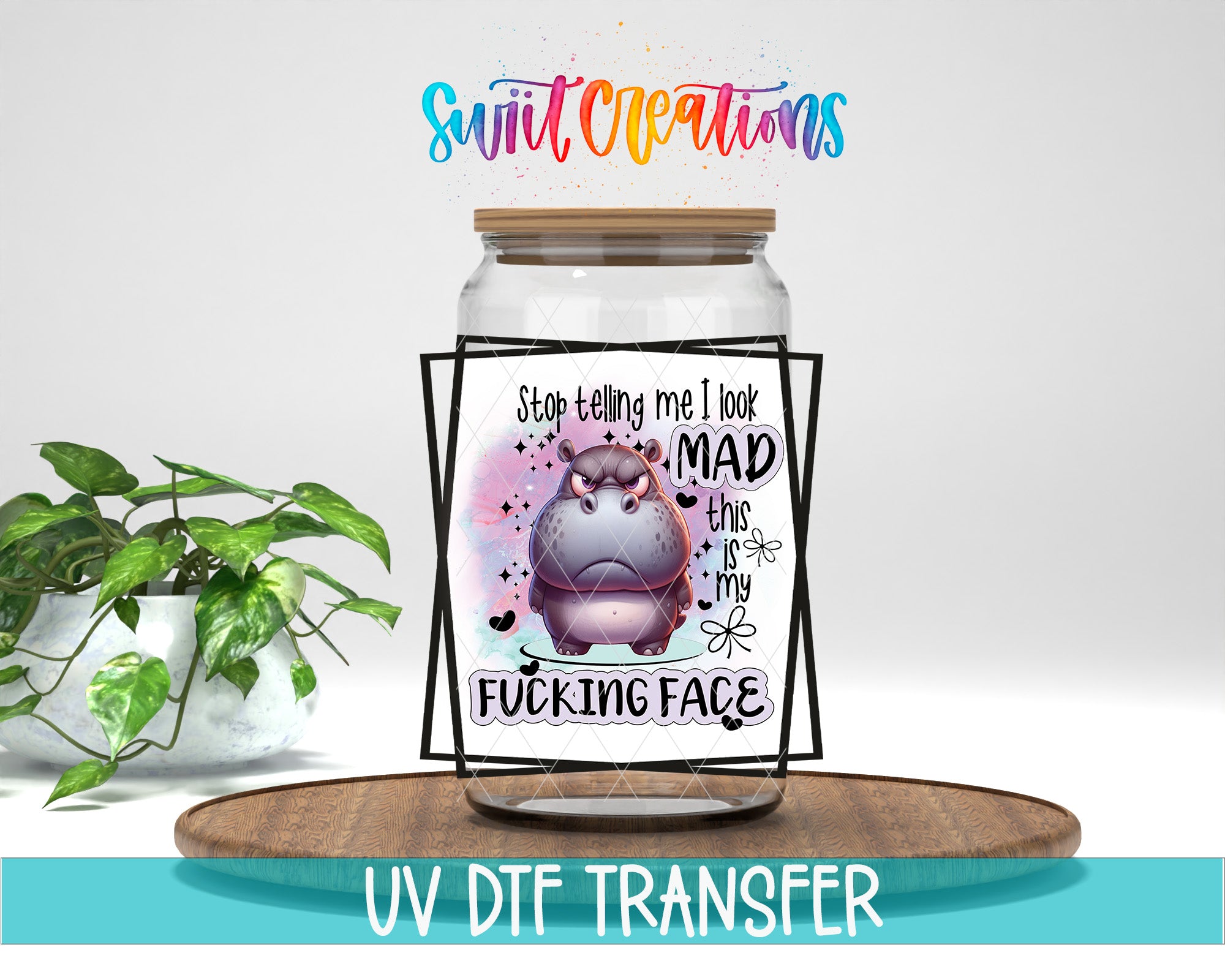 A jar with a cartoon hippo on it, accompanied by a humorous text message that reads "Stop telling me I look MAD this is my F*cking face". The jar is placed on a wooden surface, and there is a potted plant in the background.