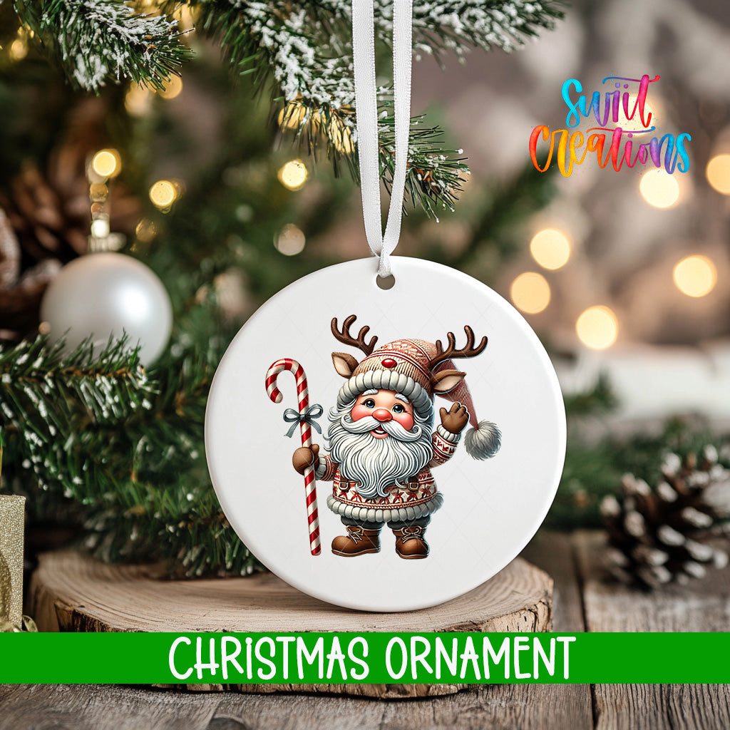 A white Christmas ornament featuring a cartoon Santa Claus holding a candy cane and reindeer antlers, hanging on a tree branch with a blurred background of Christmas lights.