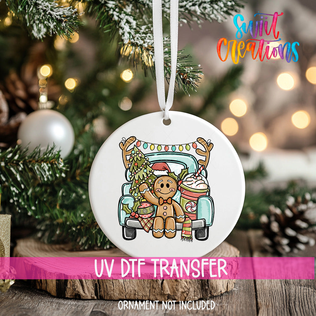 A white ornament with a gingerbread man and a truck, hanging on a Christmas tree.