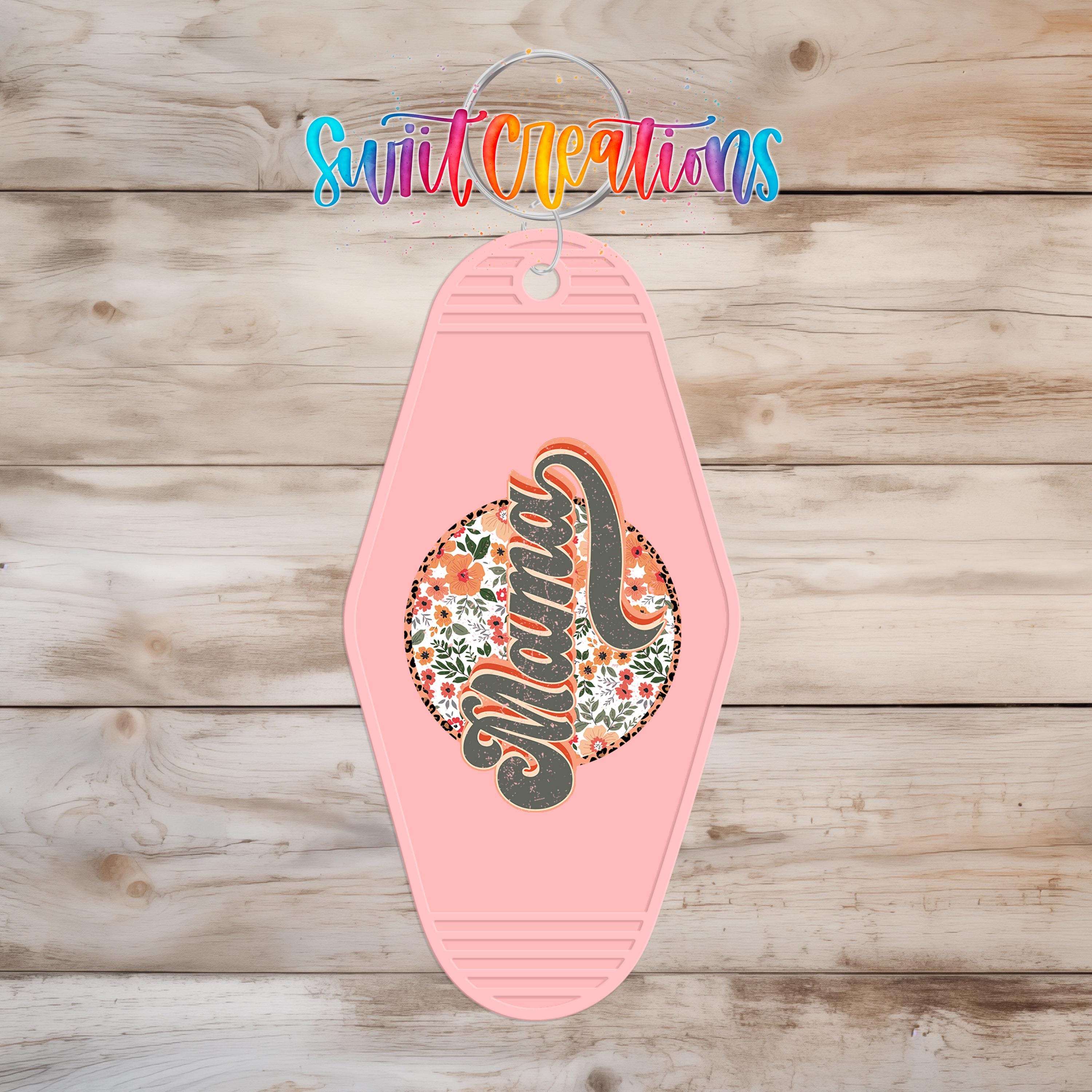A pink keychain with a floral design and the word "Mamma" printed on it, hanging on a wooden surface.