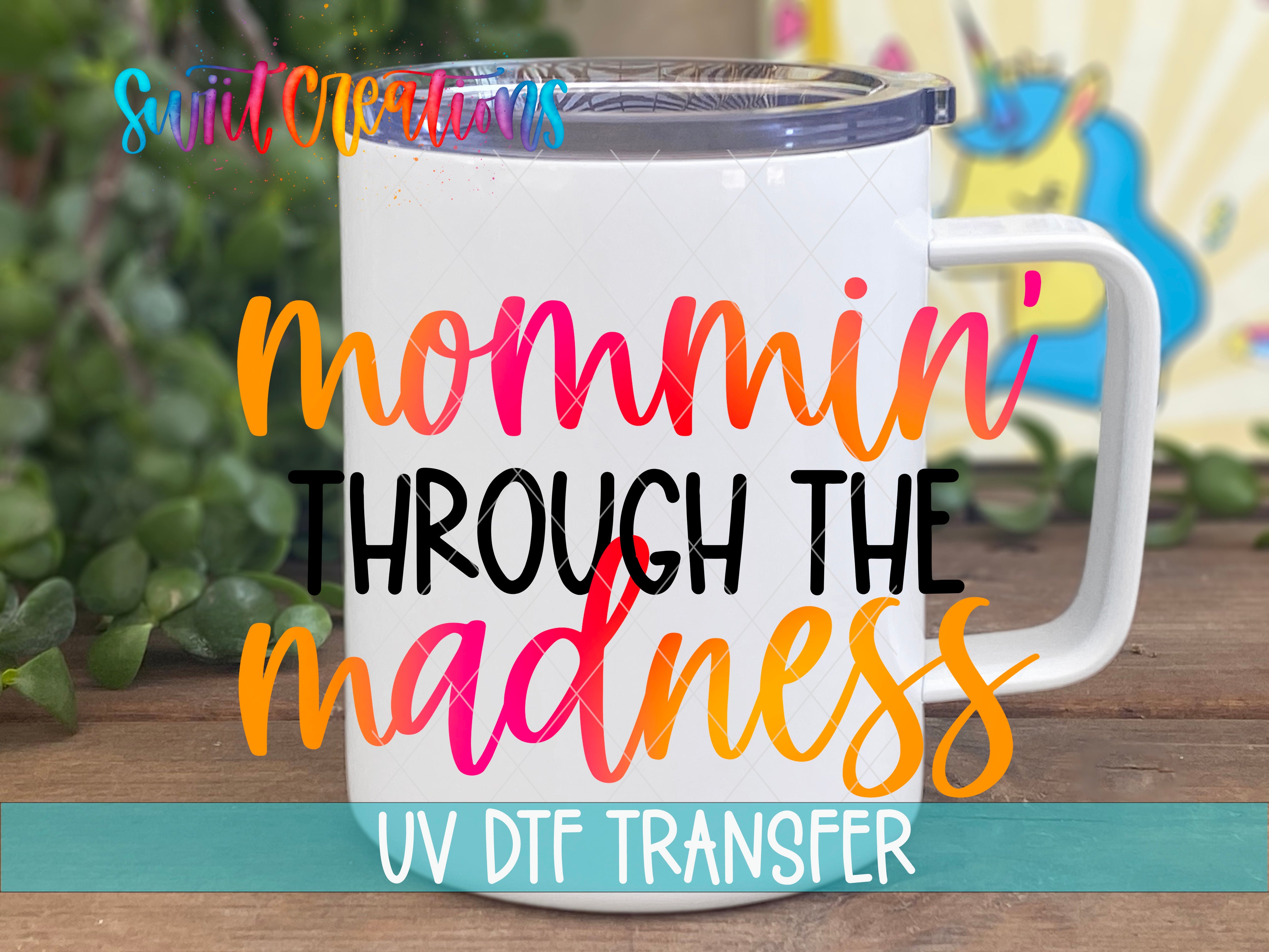 A white mug with colorful text on it, placed on a wooden surface with a blurred background.