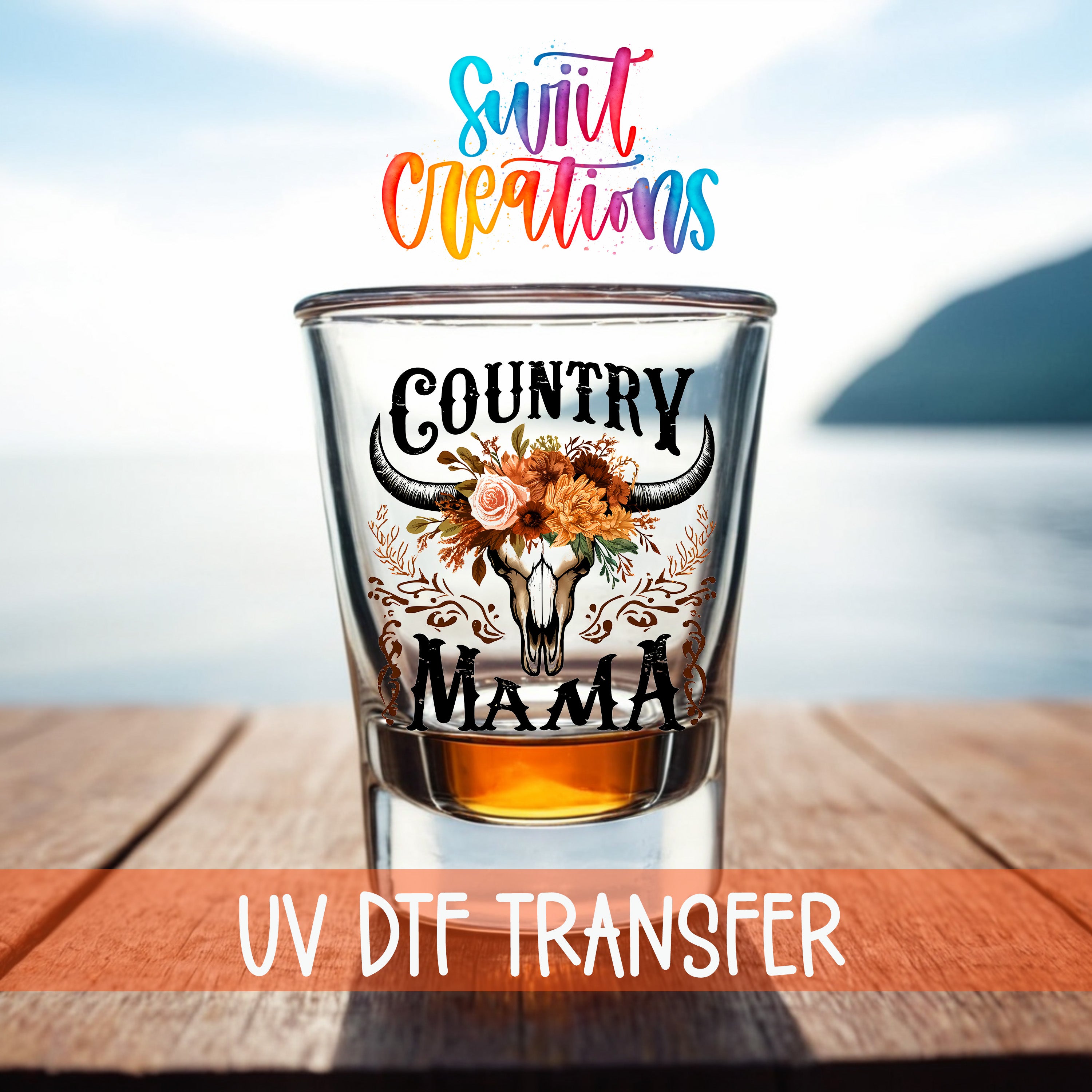 a shot glass with a floral design and the text "COUNTRY MAMA" printed on it, placed on a wooden surface with a body of water in the background.