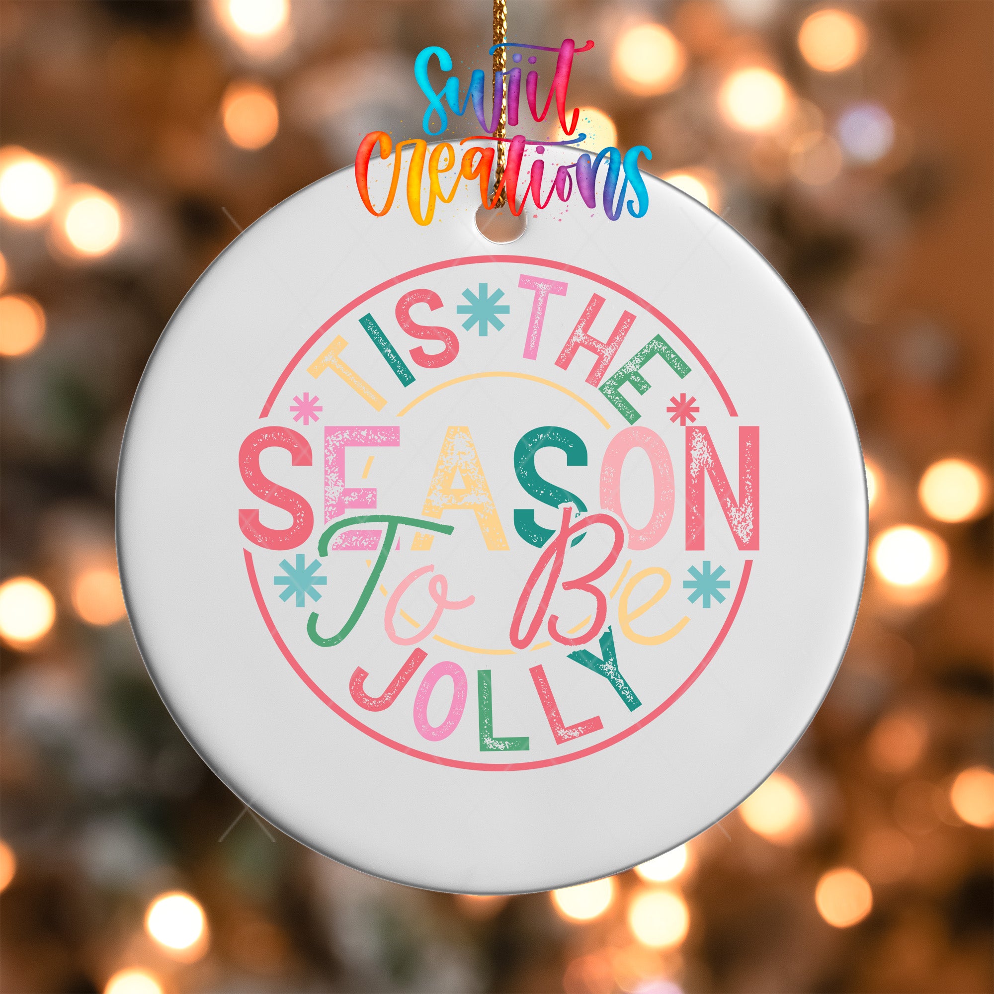 A white ornament with colorful text that says "TIS THE SEASON TO BE JOYLY" hanging on a string.