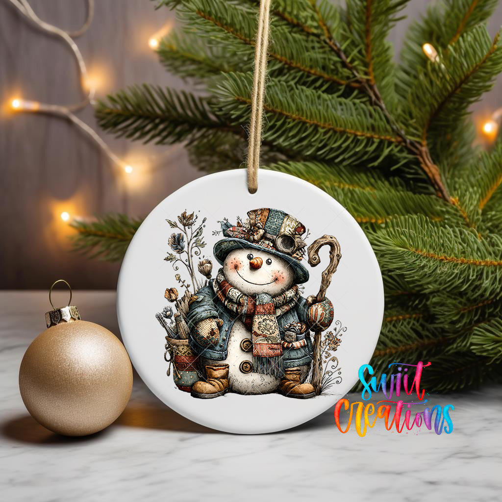 A white ceramic ornament featuring a snowman is displayed on a table, with a gold ornament and a Christmas tree in the background.