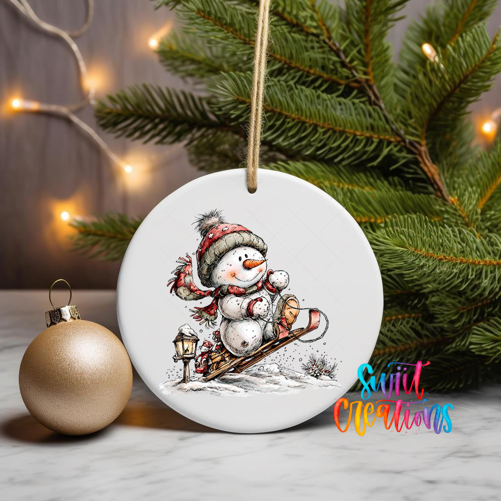 A white ceramic ornament featuring a snowman riding a sled, surrounded by a Christmas tree and twinkling lights.