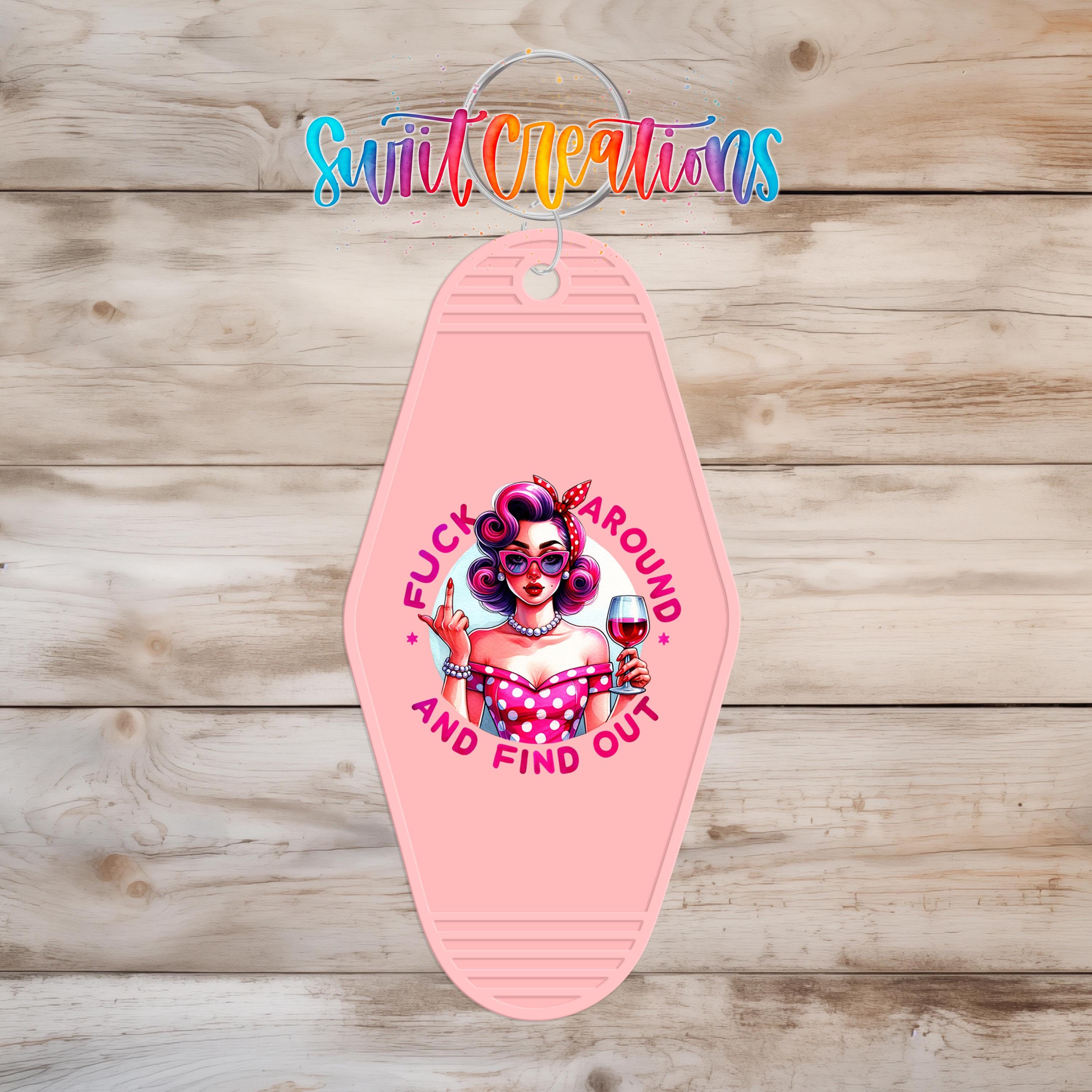 A pink keychain with a graphic design featuring a woman with curly hair and a wine glass, along with the text "FUCK AROUND AND FIND OUT".