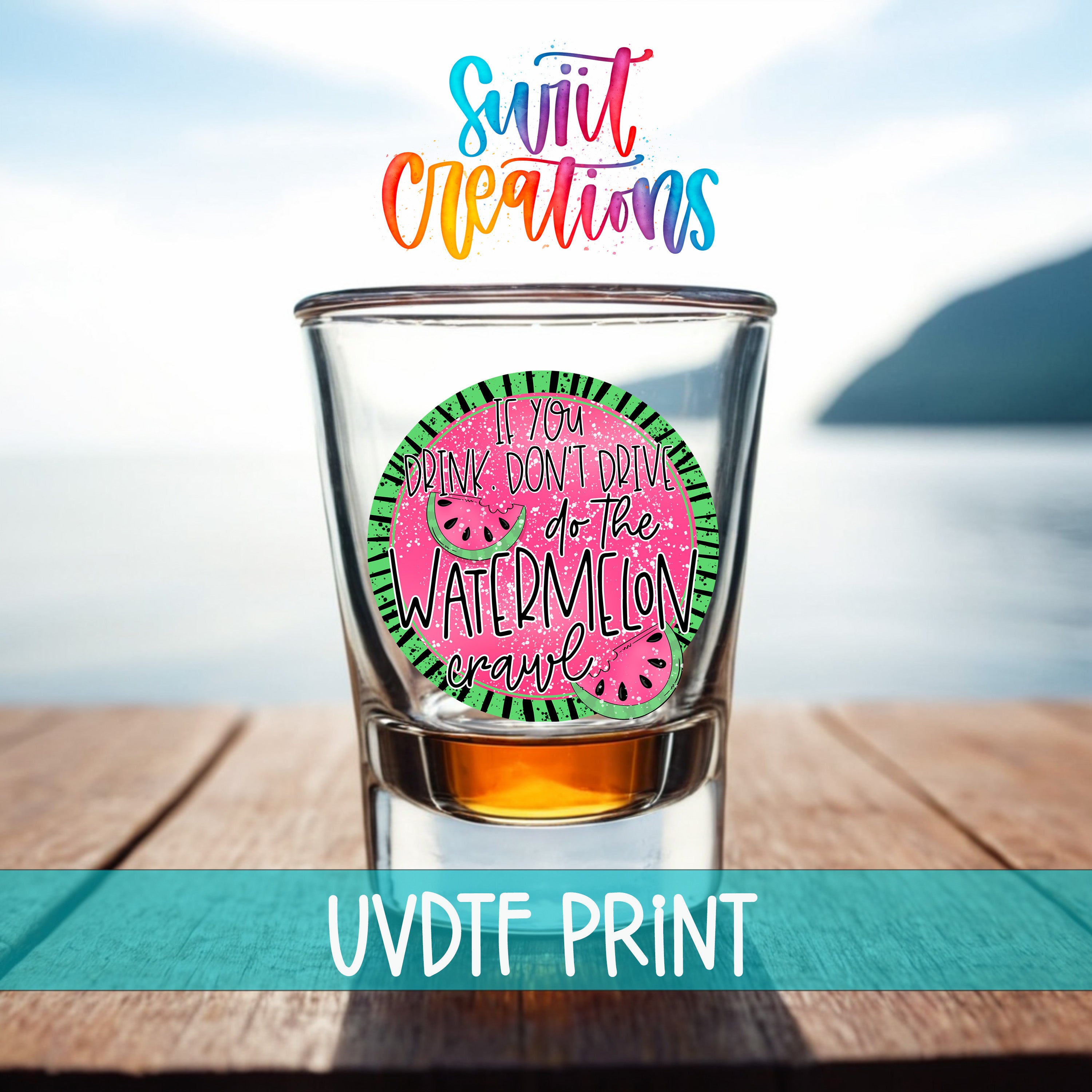 a shot glass with a watermelon design, placed on a wooden surface with a body of water in the background.