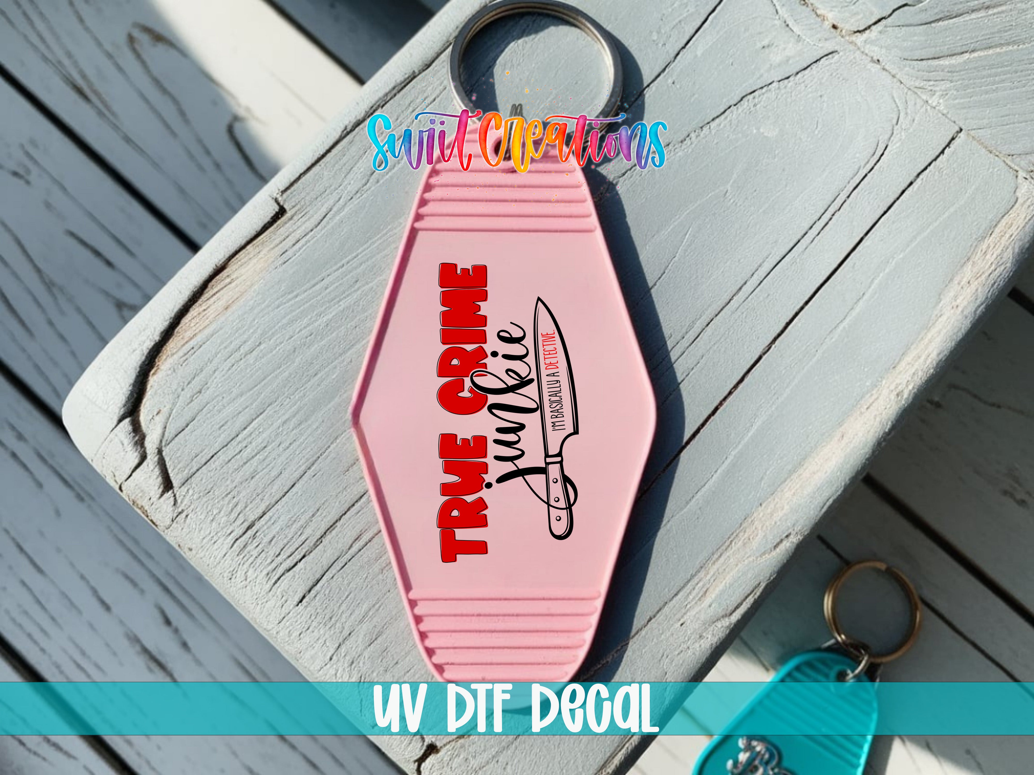 A pink keychain with the text "TRUE CRIME JUNKIE" printed on it, placed on a wooden surface.
