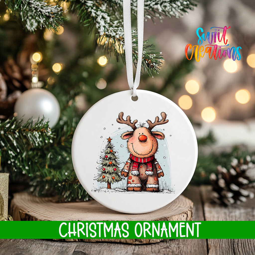 A white Christmas ornament featuring a cartoon reindeer is hanging on a tree branch, with a blurred background of pine branches and twinkling lights.