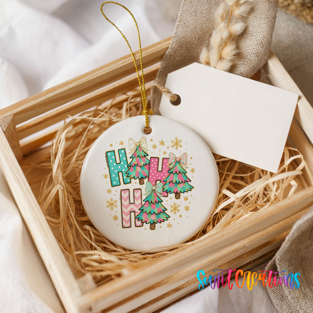 A white ceramic ornament with a colorful design, featuring the letters "H" and "H" surrounded by Christmas trees and snowflakes, placed in a wooden crate.