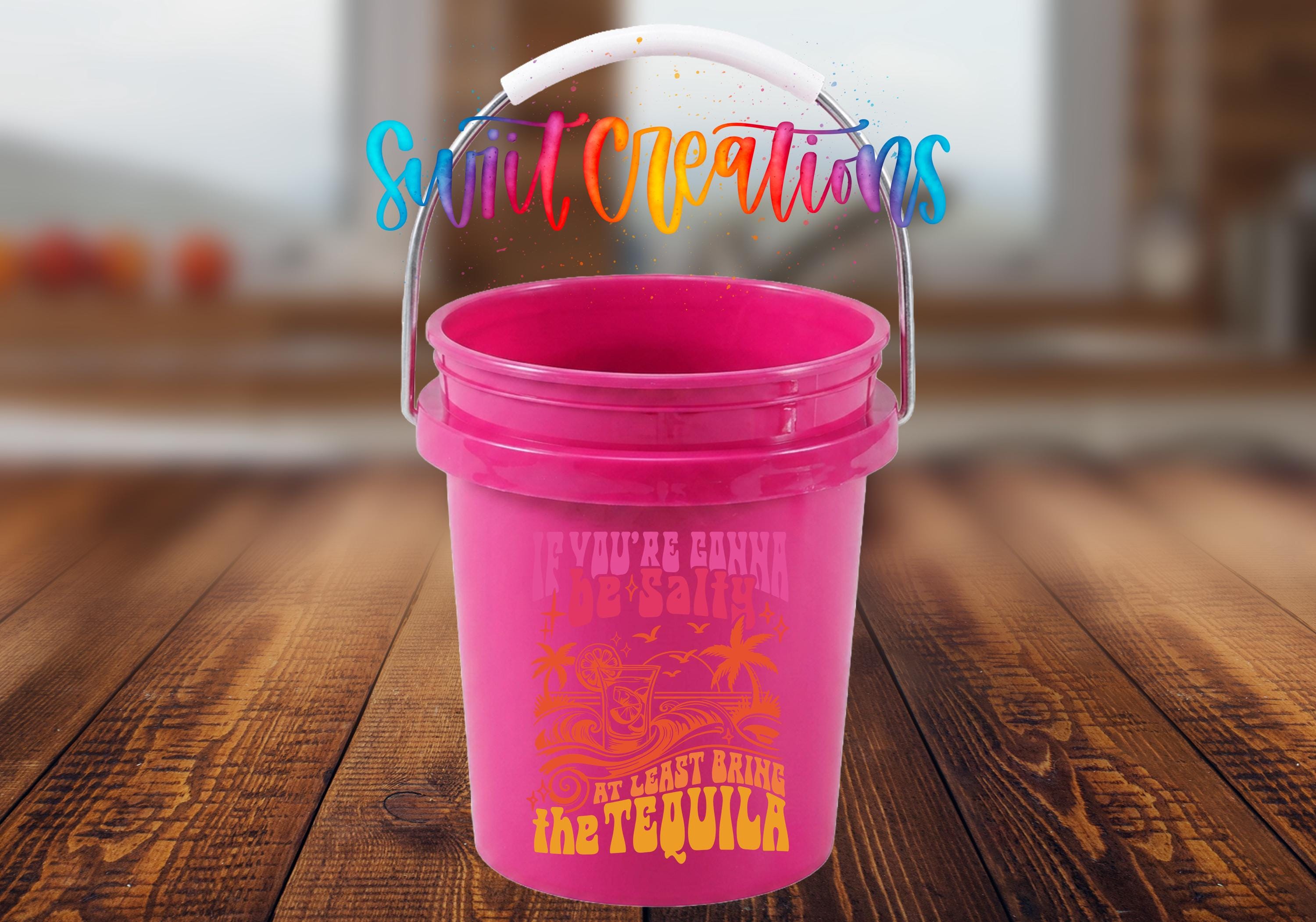 A pink plastic bucket with a handle, placed on a wooden surface.