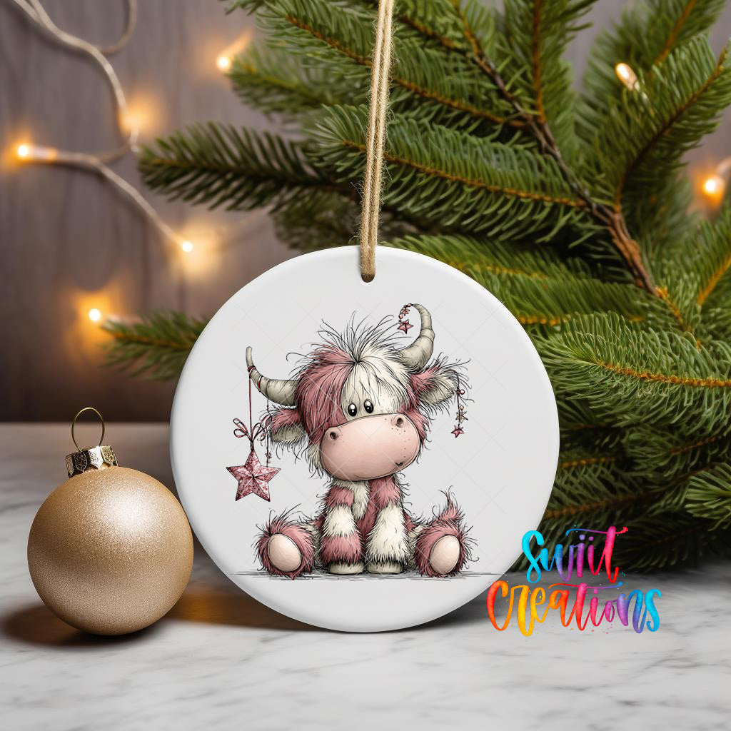 A ceramic ornament featuring a cartoon cow sitting next to a gold ornament, with a Christmas tree and twinkling lights in the background.