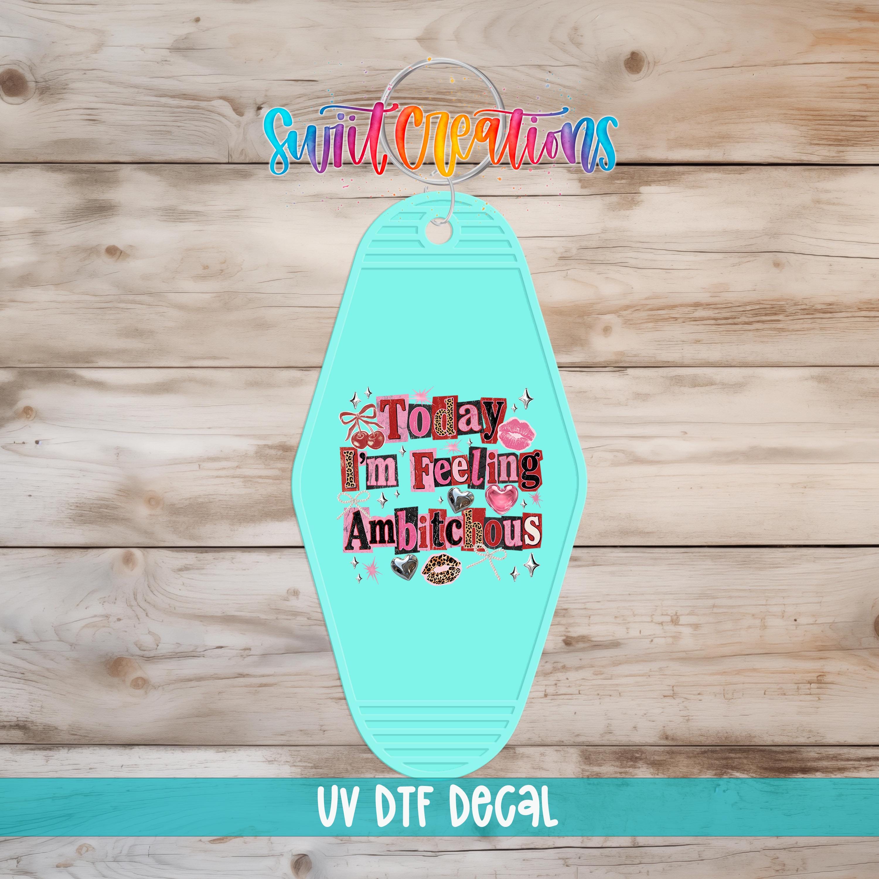 A turquoise keychain with a colorful, whimsical design and text on it, placed on a wooden surface.