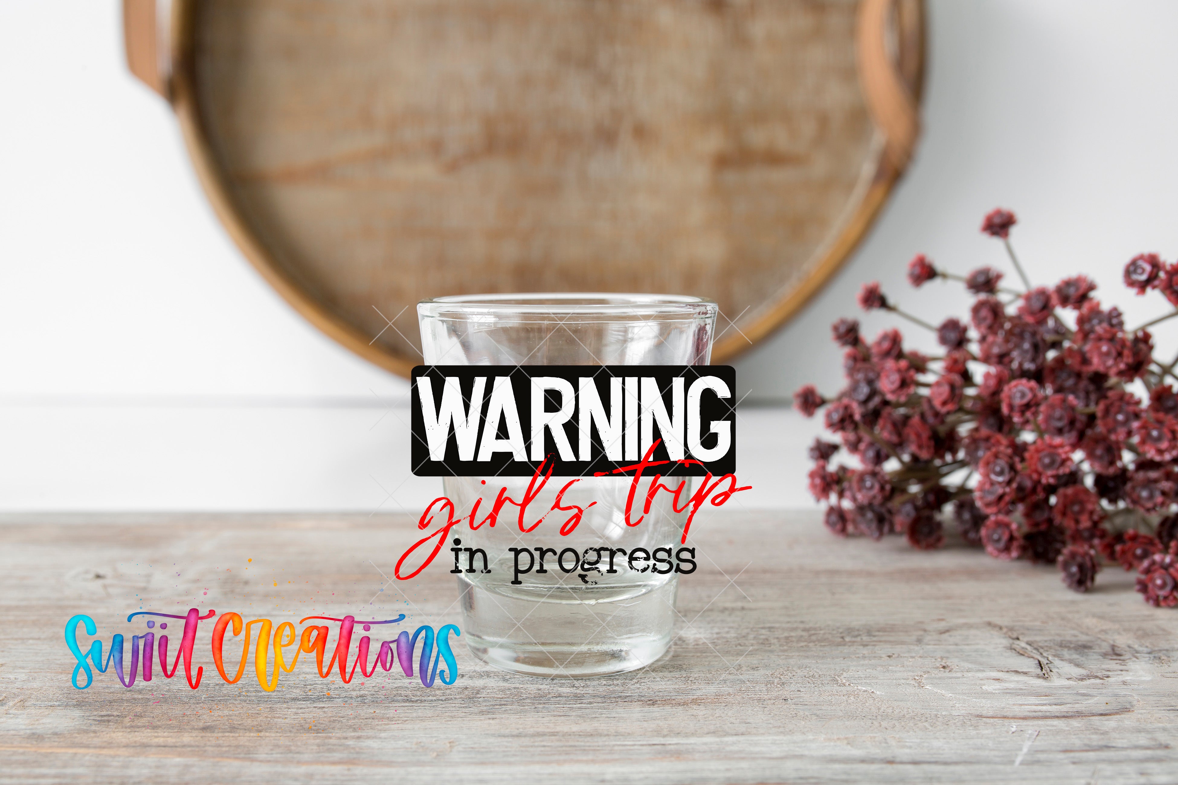a glass with a warning sign on it, placed on a wooden surface next to a bunch of red flowers.
