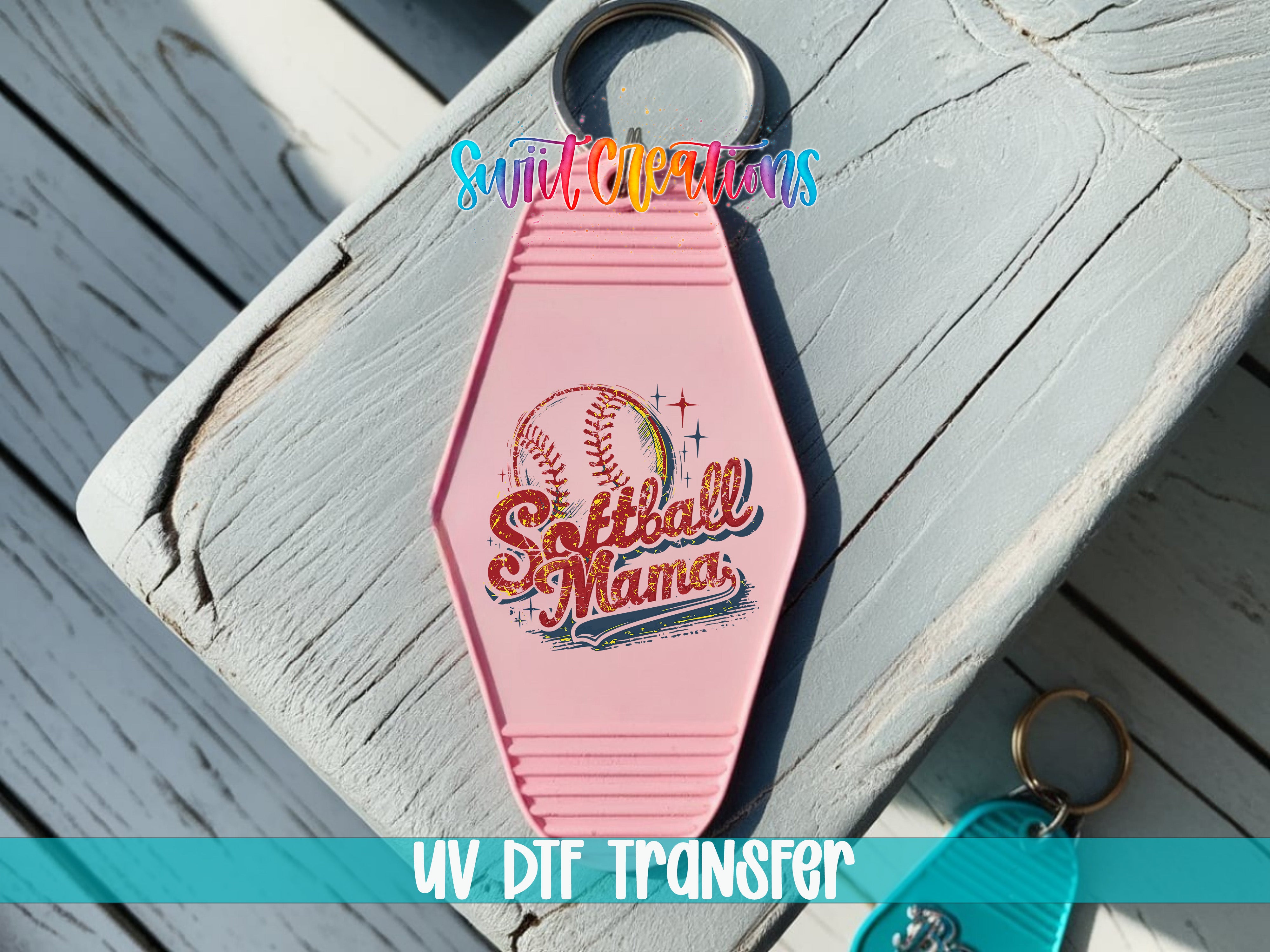 A pink keychain with the text "Softball Mama" printed on it, sitting on a wooden surface.