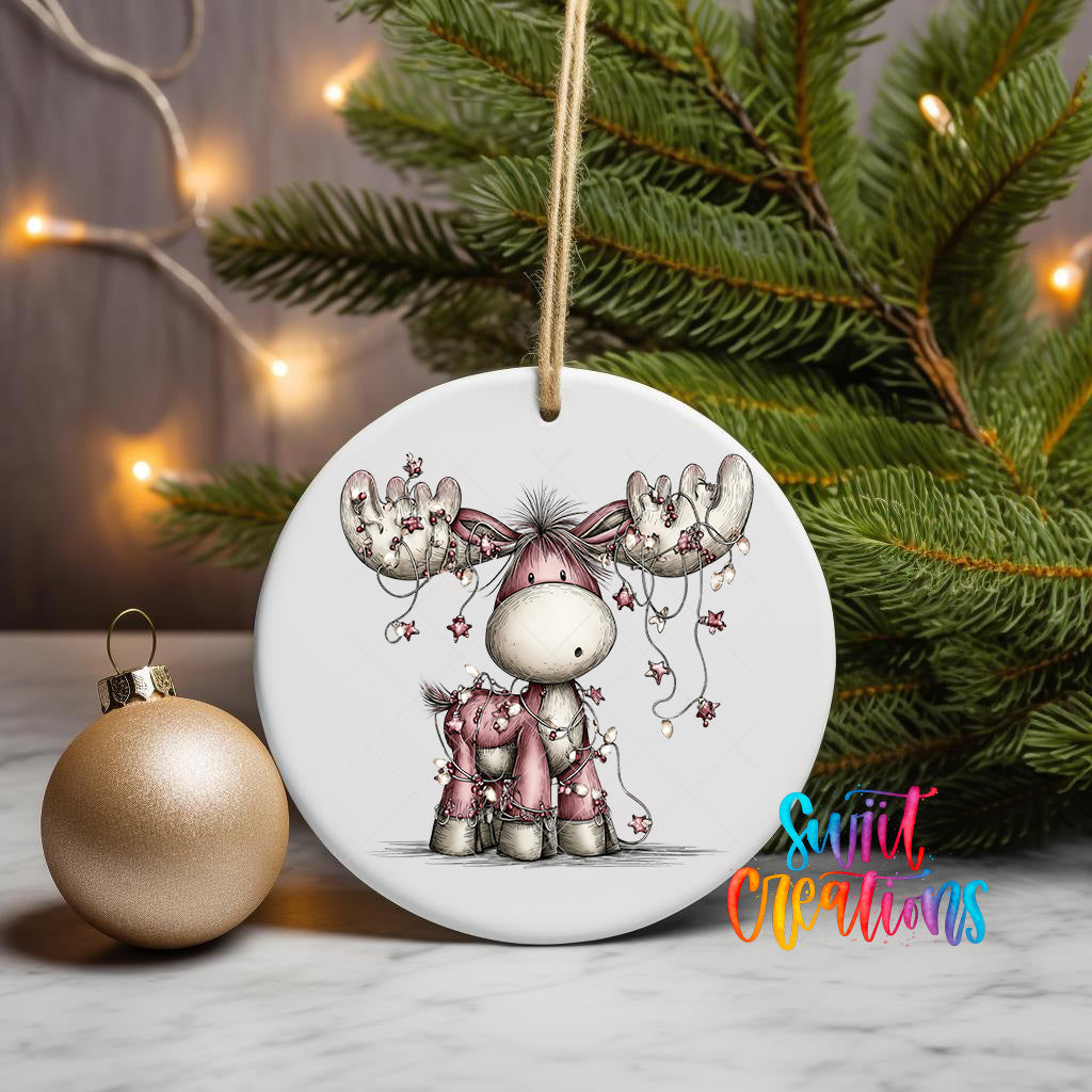 A white ceramic ornament featuring a cartoon moose and a deer, with Christmas lights in the background.