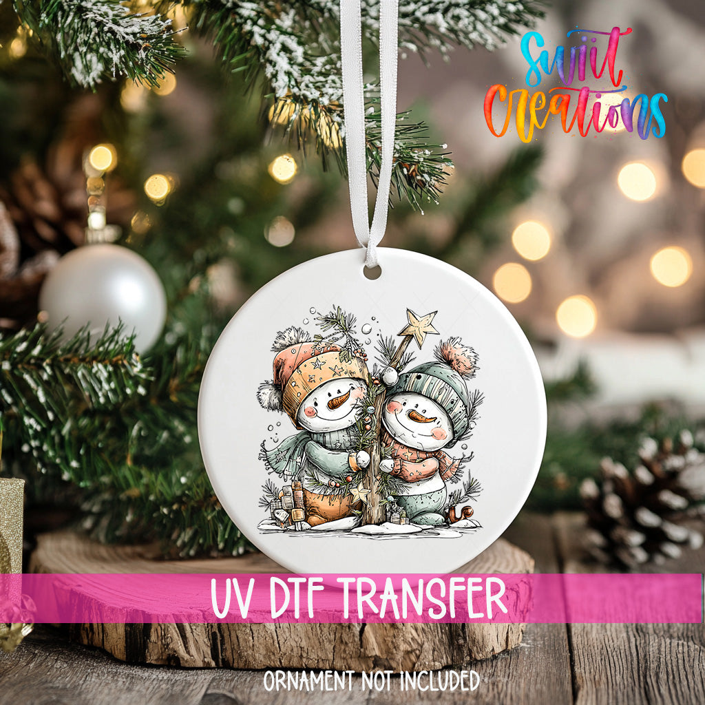 A white ceramic ornament with a snowman and star on a Christmas tree, with a pink ribbon around it.