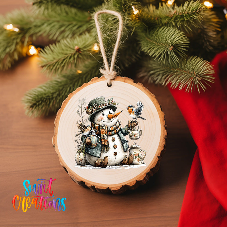 A wooden ornament featuring a snowman holding a bird, surrounded by pine branches and twinkling lights, hangs on a Christmas tree.