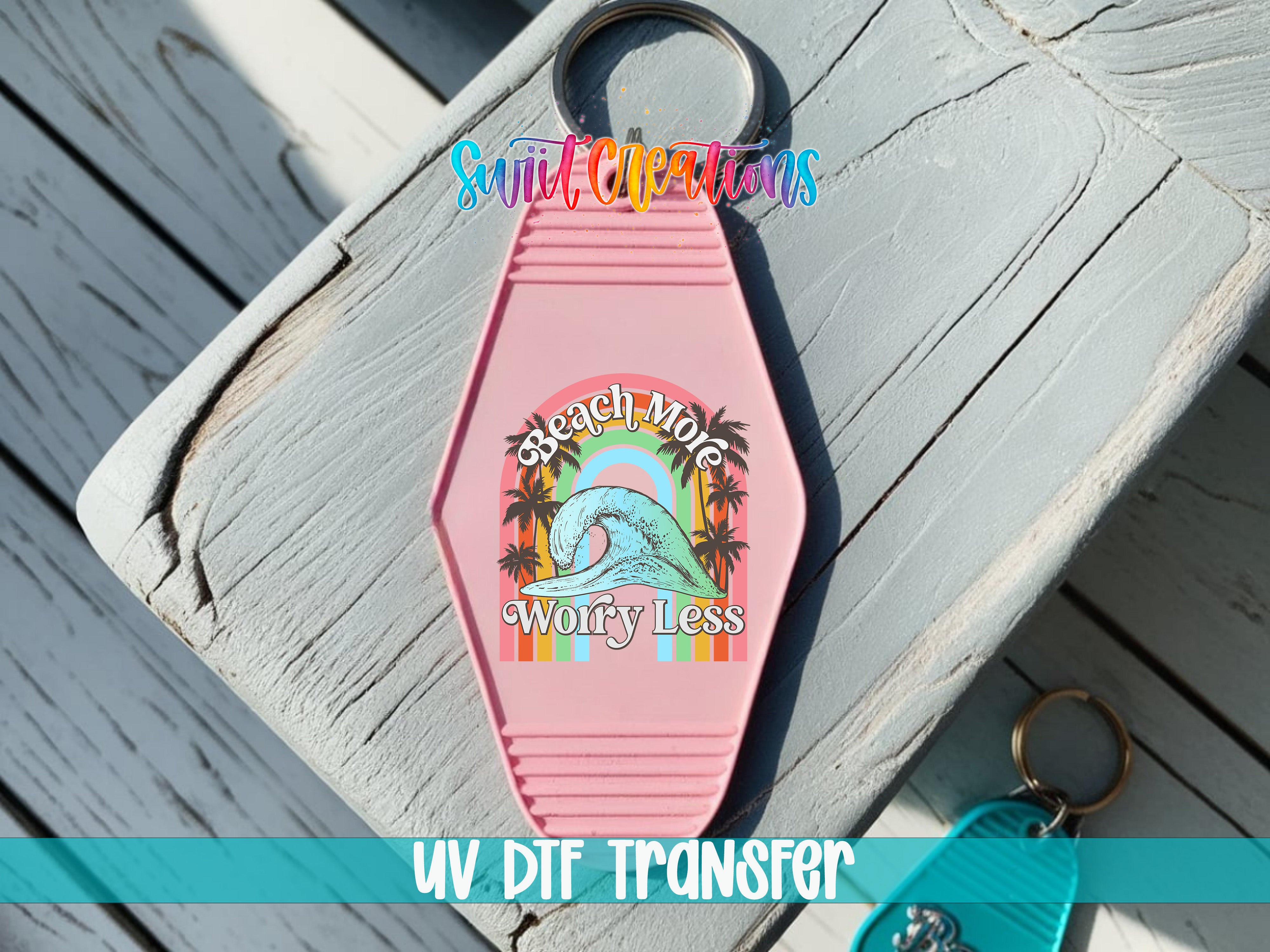A pink keychain with a colorful graphic design and text, placed on a wooden surface.