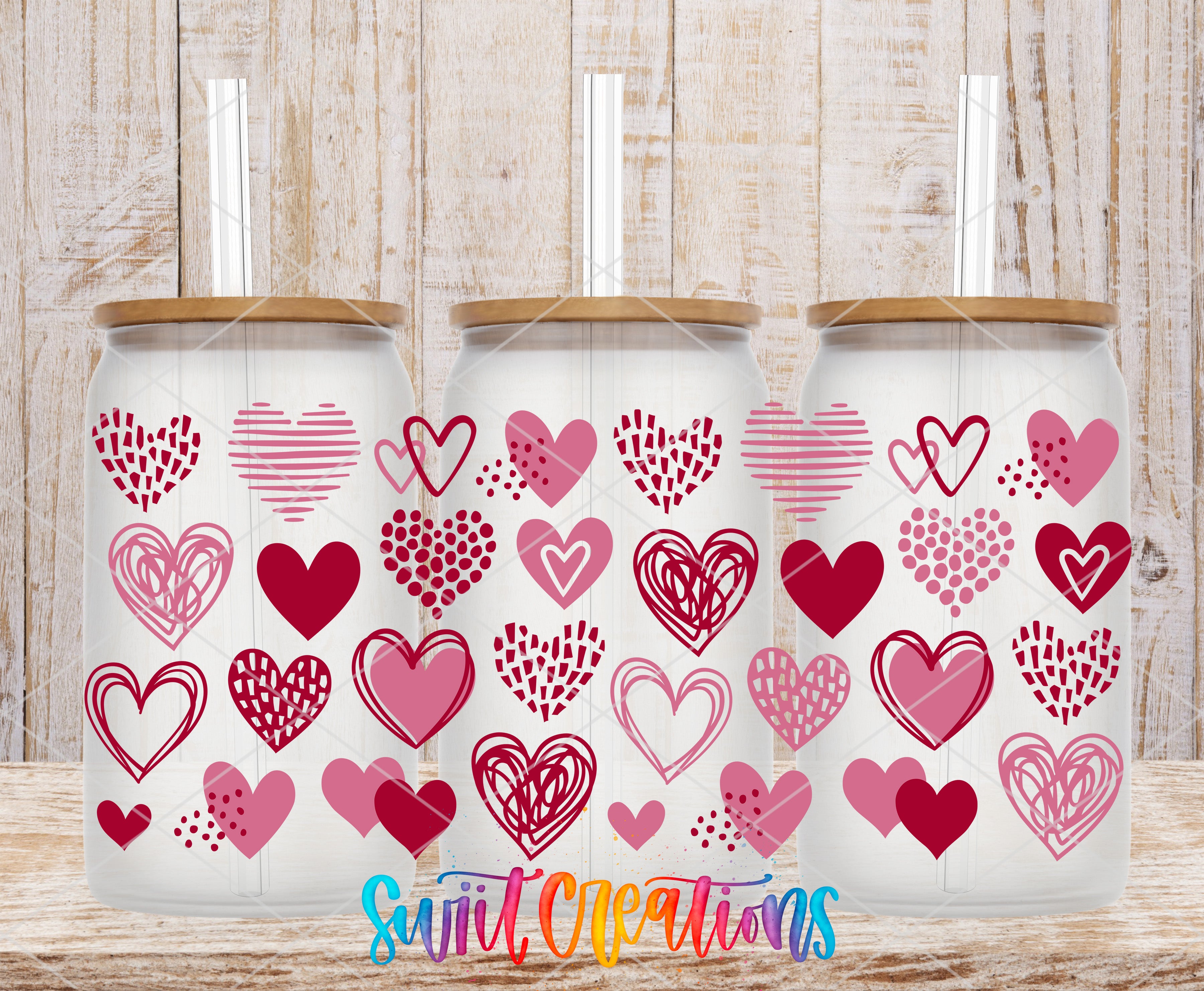 Three glass tumblers with heart-shaped designs on them, placed on a wooden surface.
