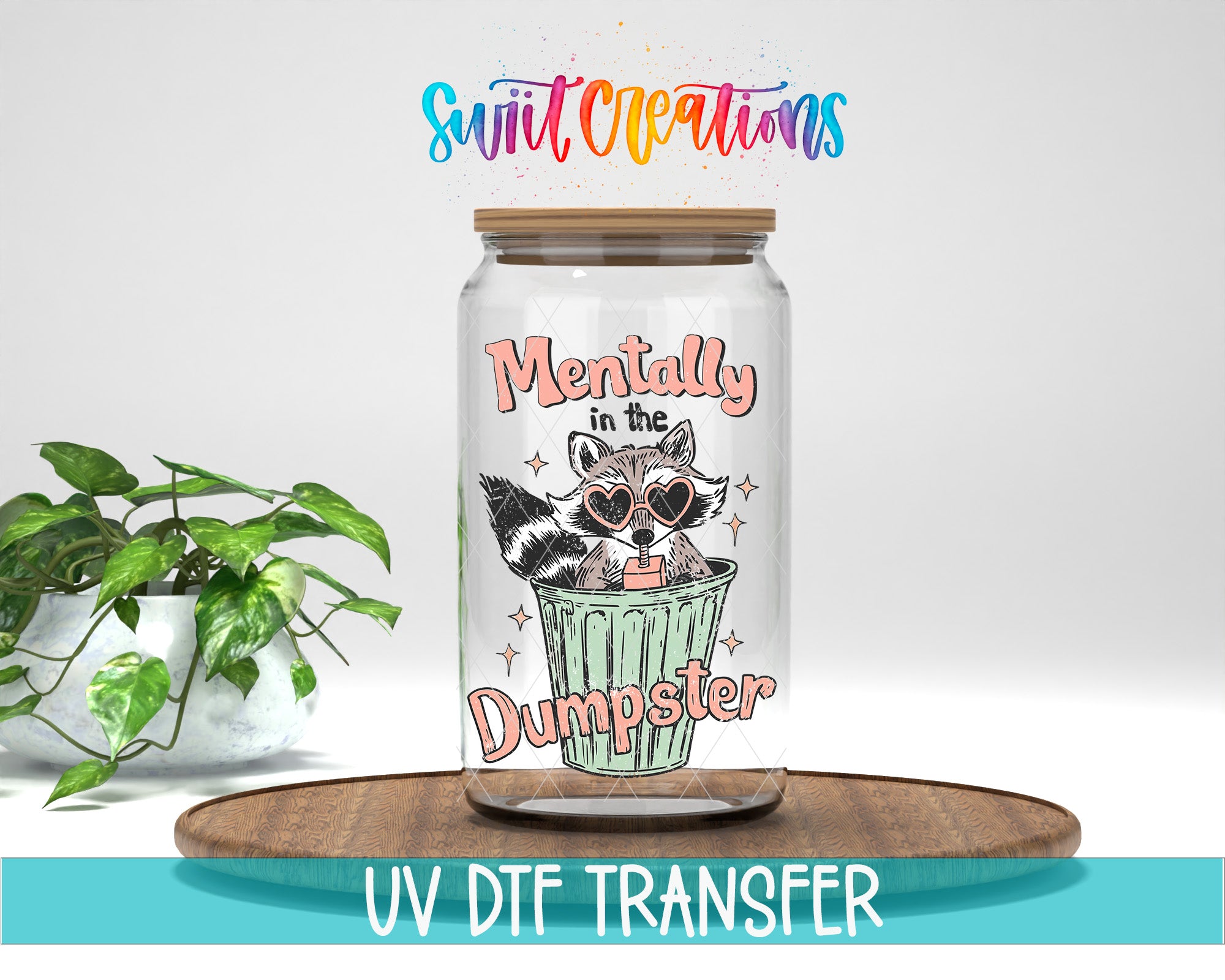 a glass jar with a raccoon wearing sunglasses and the text "Mentally in the Dumpster" printed on it, placed on a wooden surface.