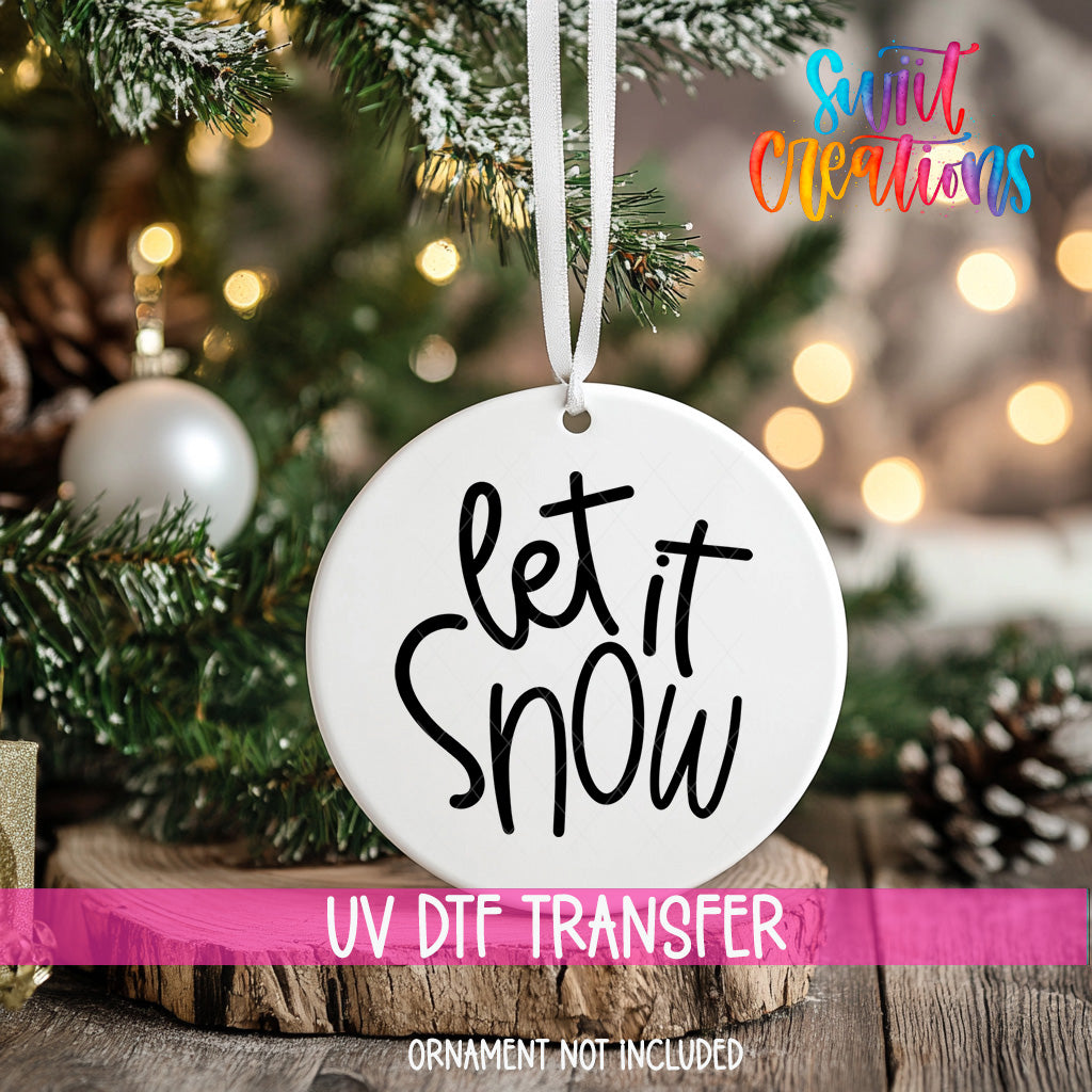 A white ornament with the text "let it snow" hanging from a Christmas tree.
