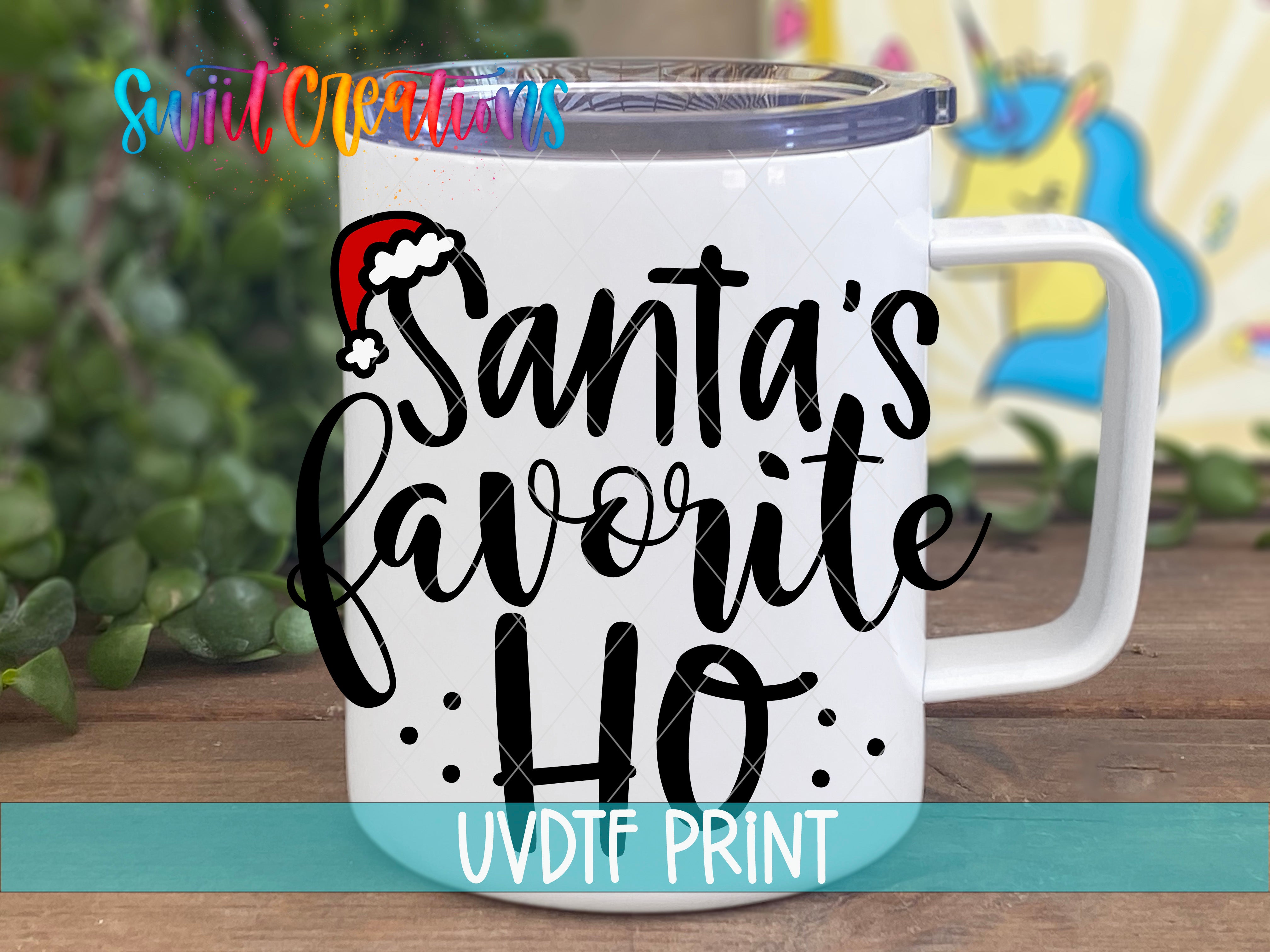 A white mug with a printed text that says "Santa's favorite ho" on it, placed on a wooden surface with a blurred background.